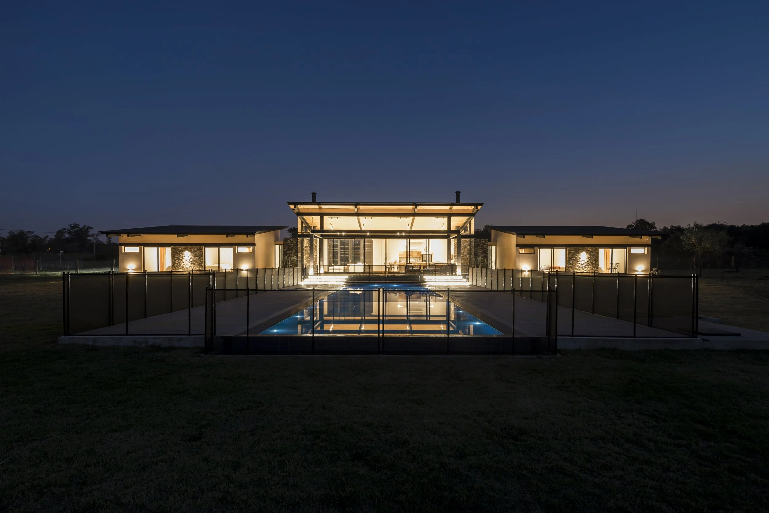 Casa moderna iluminada con piscina reflejante, en la noche.
