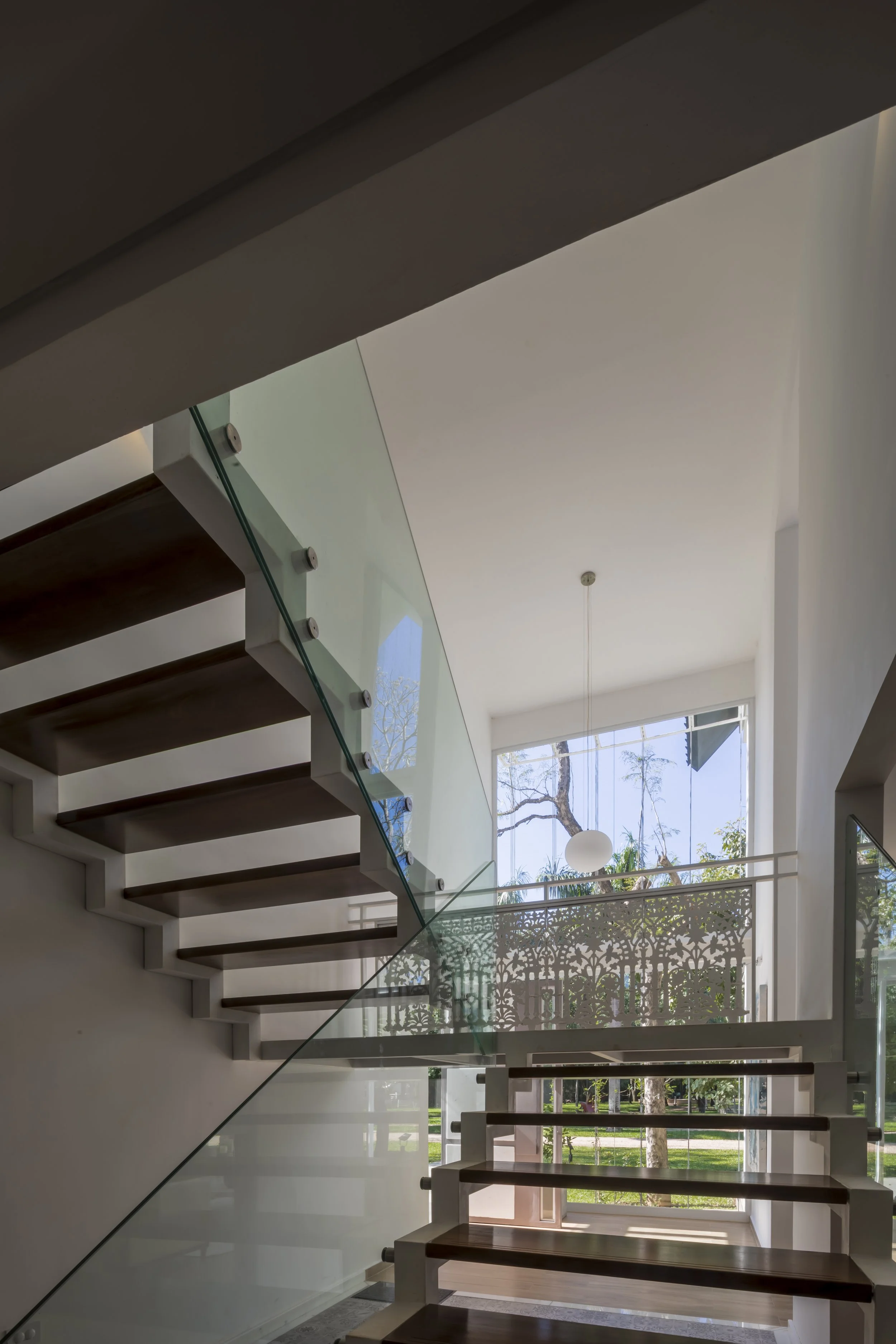 Escalera moderna con peldaños de madera, barandal de vidrio y vista al exterior con árboles y jardín.