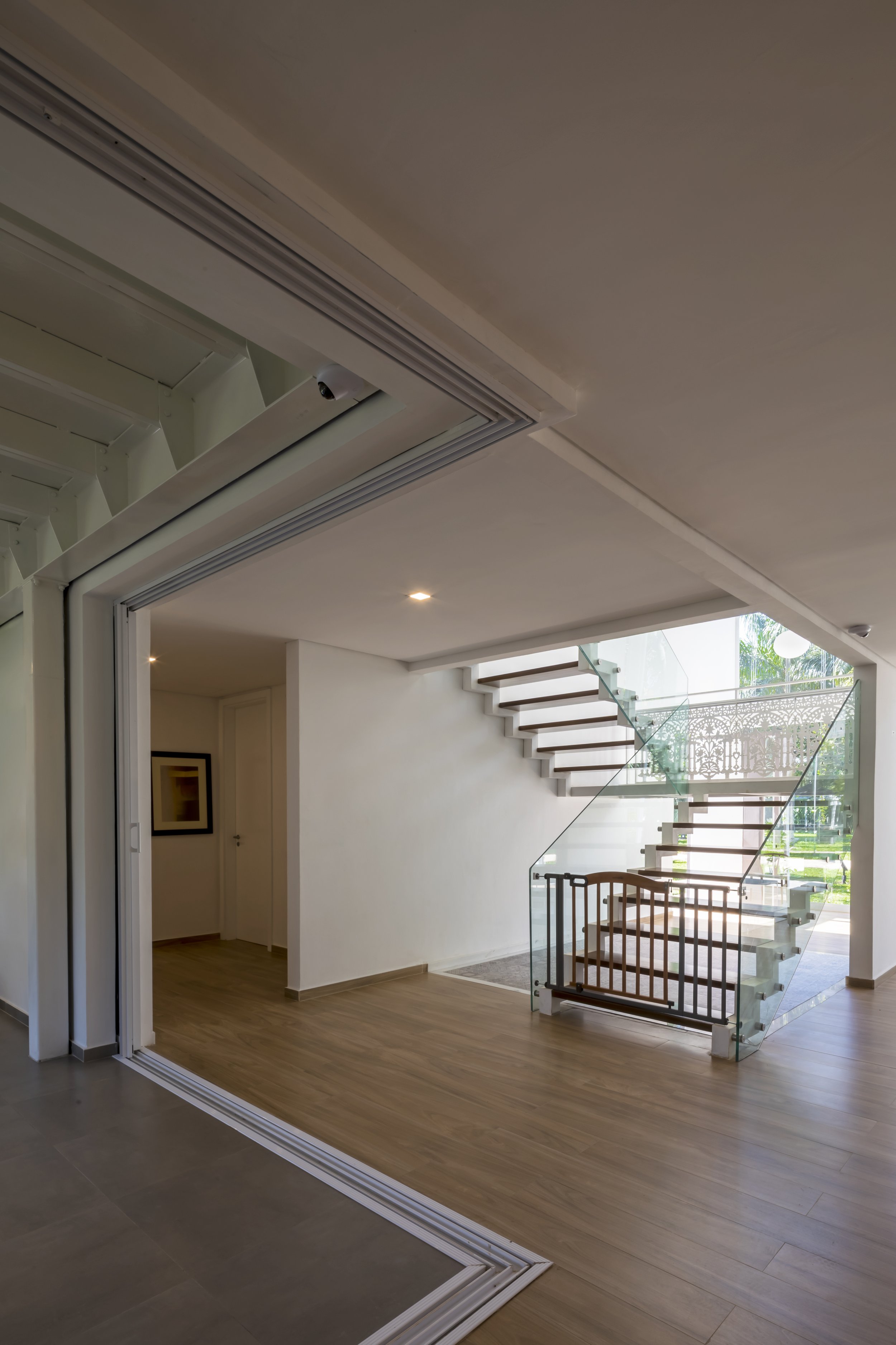 Vista interior de una casa moderna con escalera de vidrio y madera, suelo de madera y puertas corredizas.