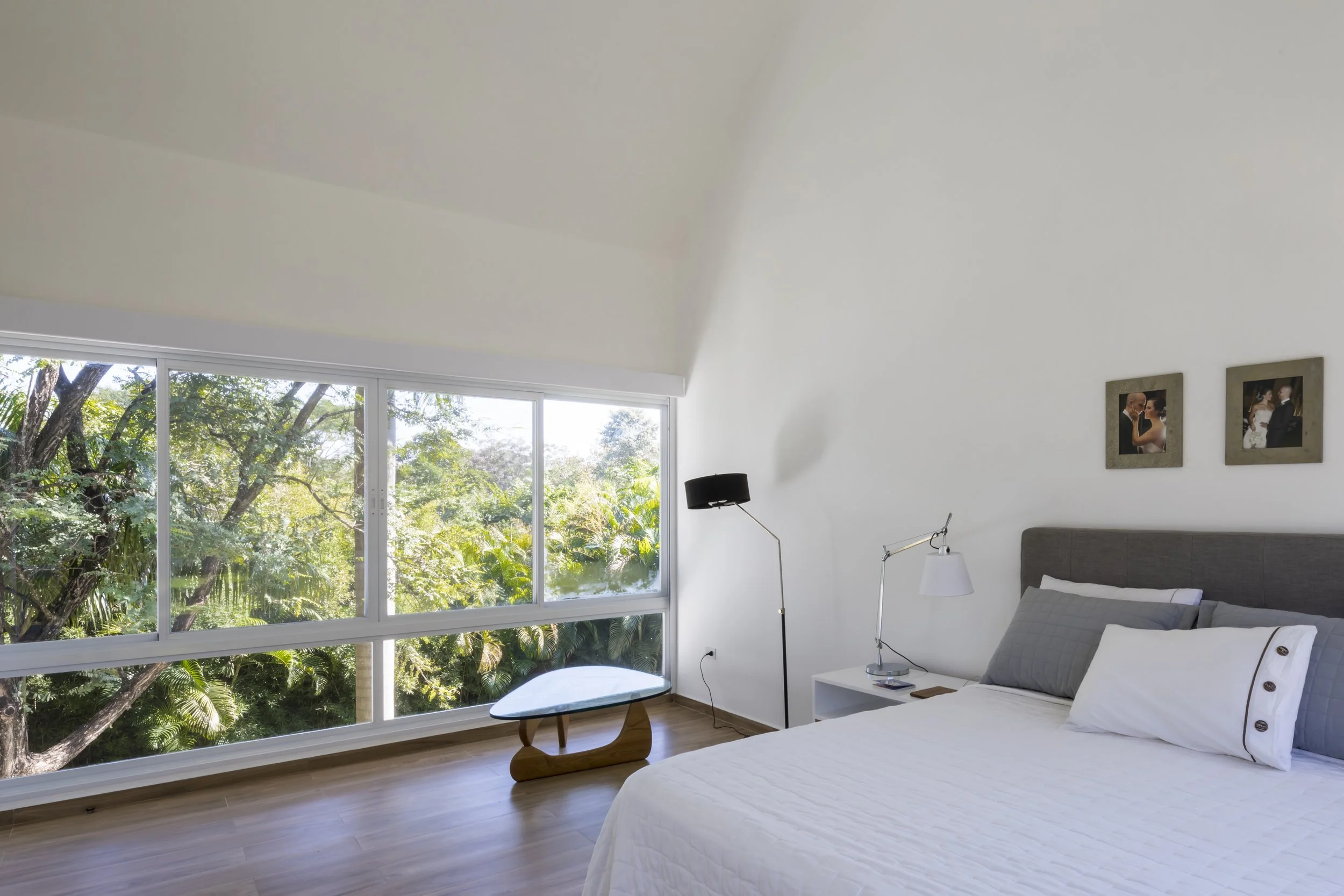 Habitación moderna con vista a un bosque, cama con ropa blanca, lámparas y cuadros en la pared