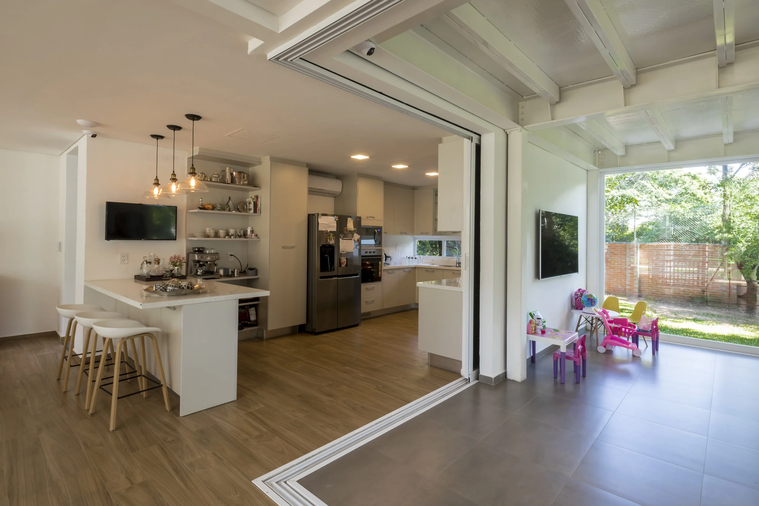 Vista de una cocina moderna y una sala de juegos infantil en una casa, con espacio abierto y paredes blancas.