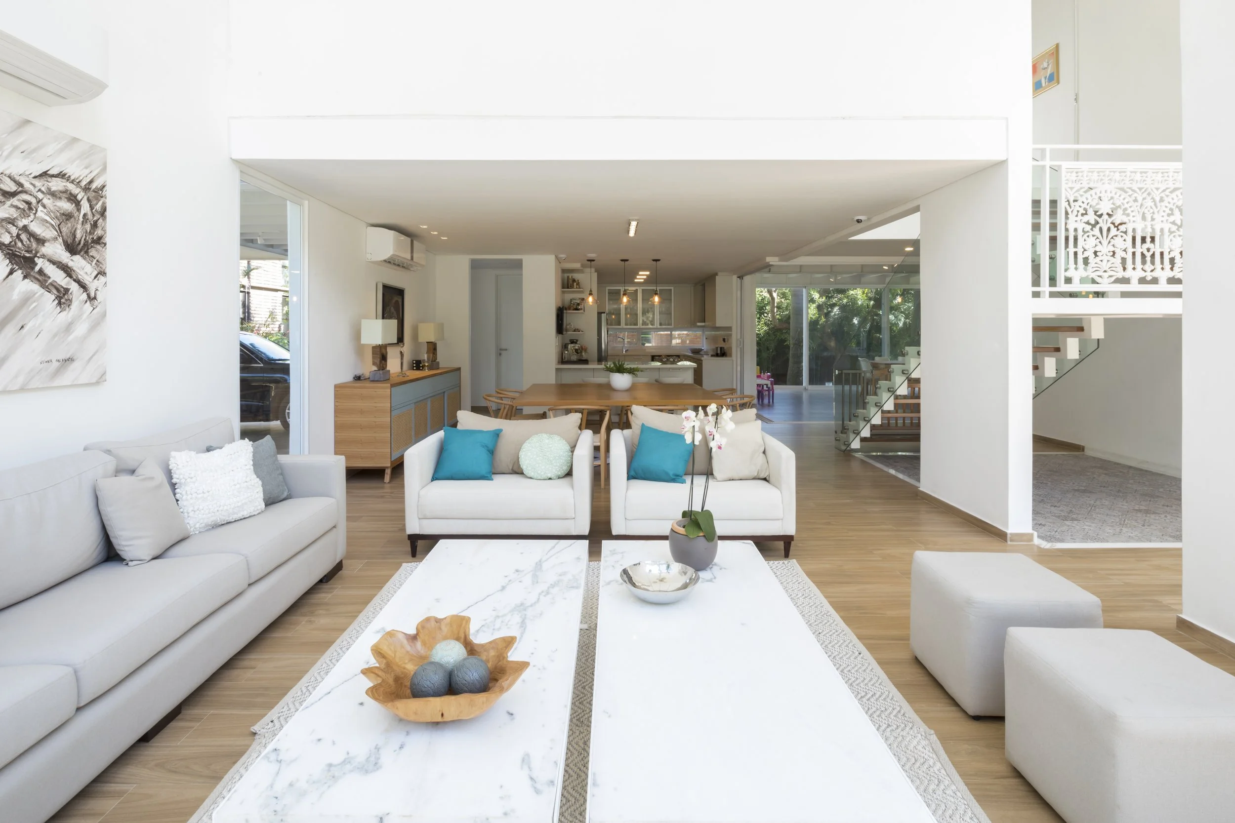 Sala de estar moderna con muebles blancos, cojines azules, mesa de centro de mármol y decoraciones elegantes.