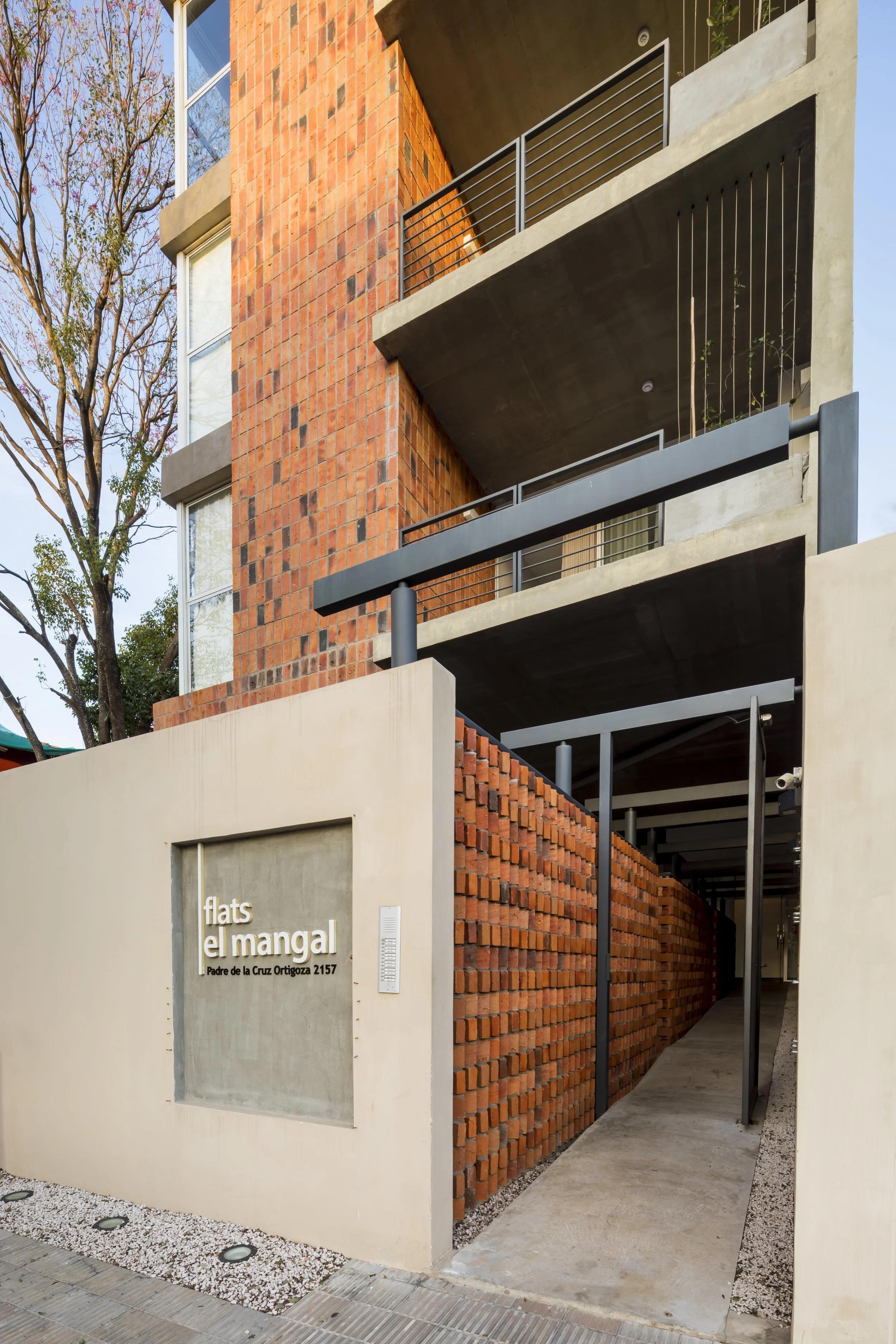 Fachada de edificio moderno con paredes de ladrillo y concreto, con un cartel que dice 'flats el mangal' en la entrada
