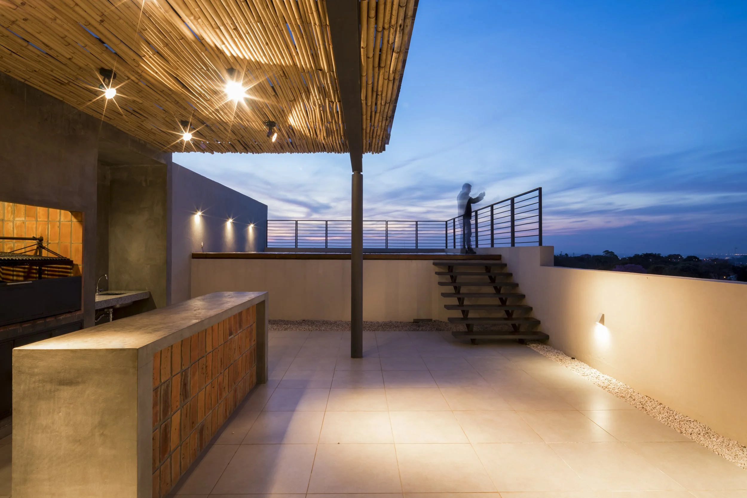 PRO ARQUITECTURA PARAGUAY architecture design PROSA
Terraza moderna al atardecer con iluminación y vista panorámica, mostrando a una persona usando un teléfono móvil