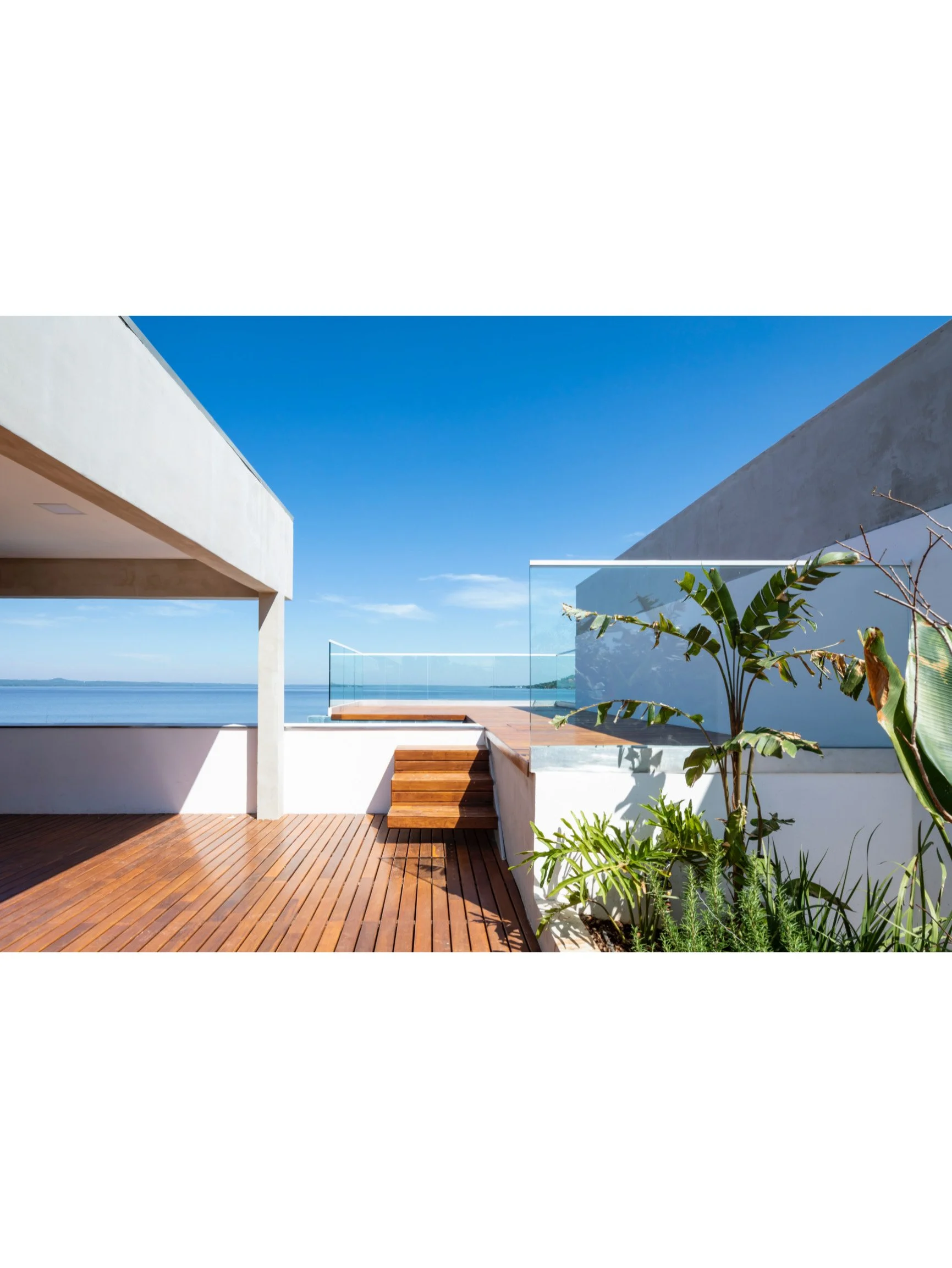 PRO ARQUITECTURA PARAGUAY architecture design PROSA
Terraza moderna con vista al mar, plantas verdes, suelo de madera y paredes blancas bajo cielo despejado.