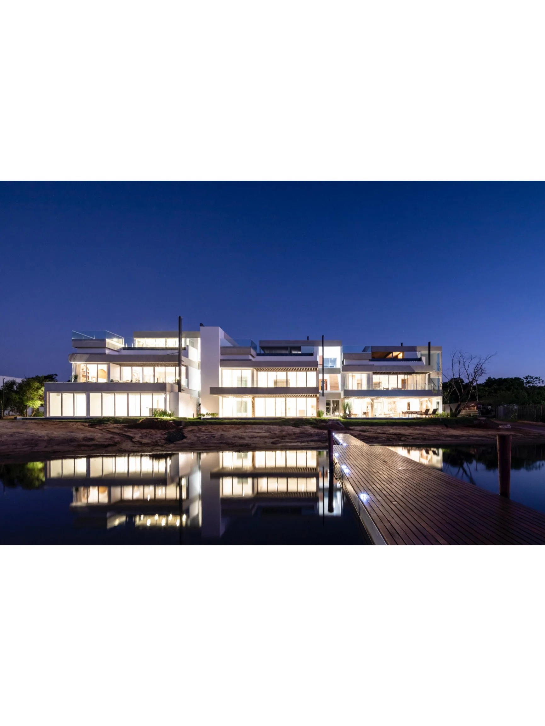 PRO ARQUITECTURA PARAGUAY architecture design PROSA
Edificio moderno y luminoso en la noche, reflejado en un cuerpo de agua, con un muelle de madera iluminado.