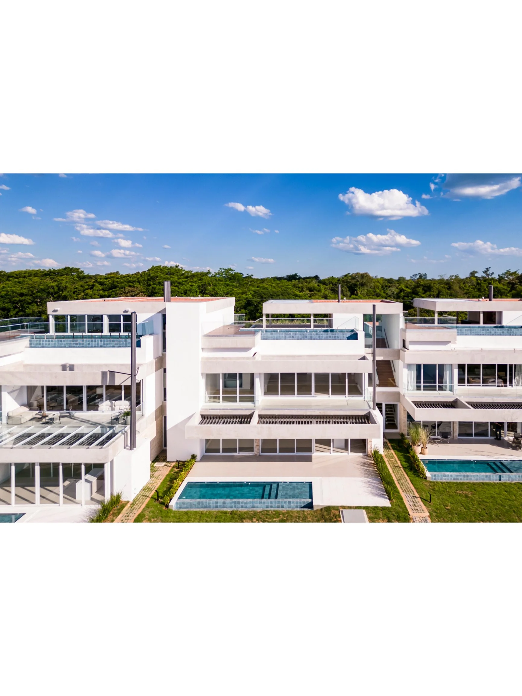 PRO ARQUITECTURA PARAGUAY architecture design PROSA
Vista aérea de un complejo de apartamentos modernos blancos con piscinas y áreas verdes, rodeado de árboles y cielo azul con nubes.