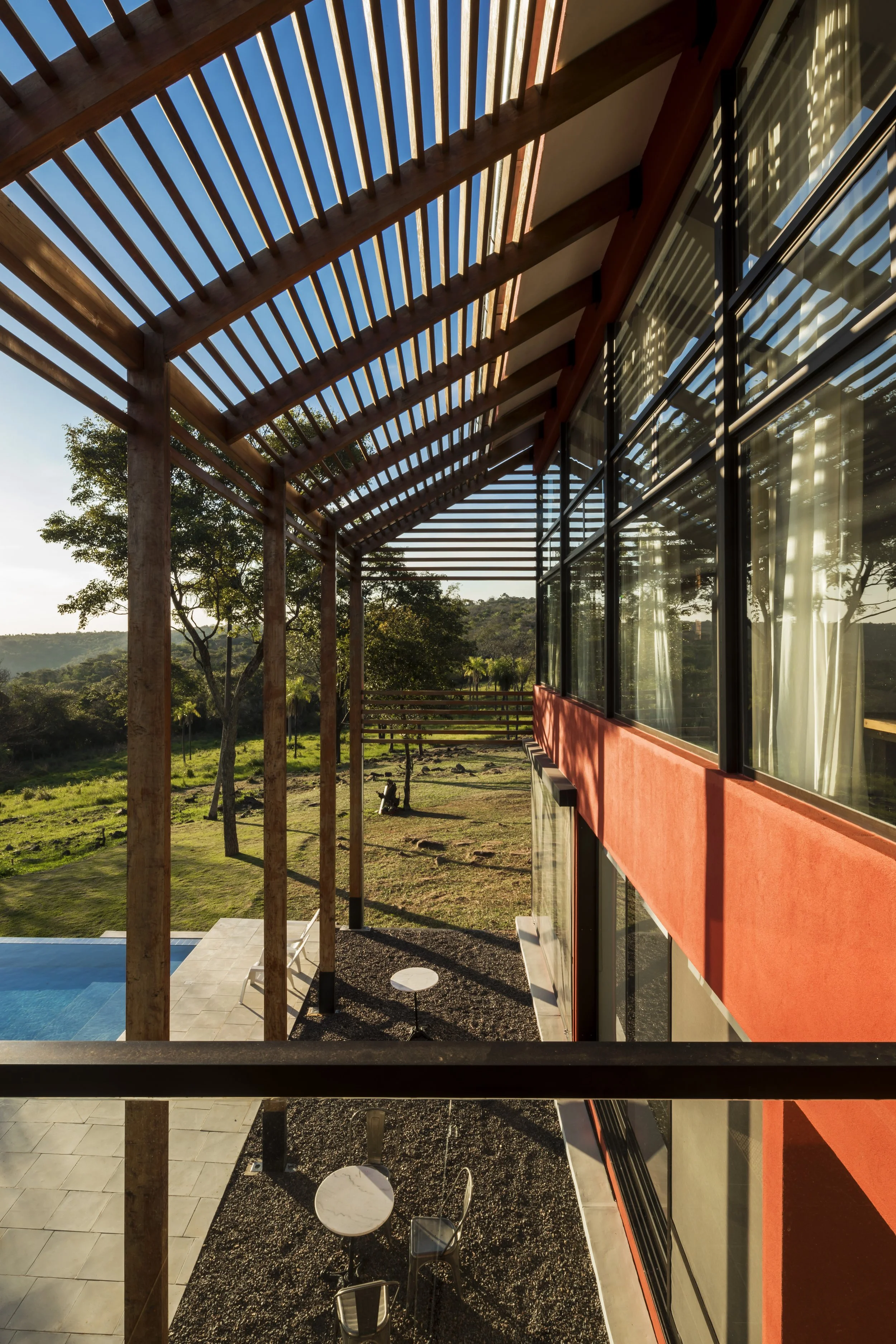 PRO ARQUITECTURA PARAGUAY architecture design PROSA
Vista desde un balcón de una casa moderna con estructura de madera y grandes ventanas, con un campo y árboles al fondo, y una piscina al lado.