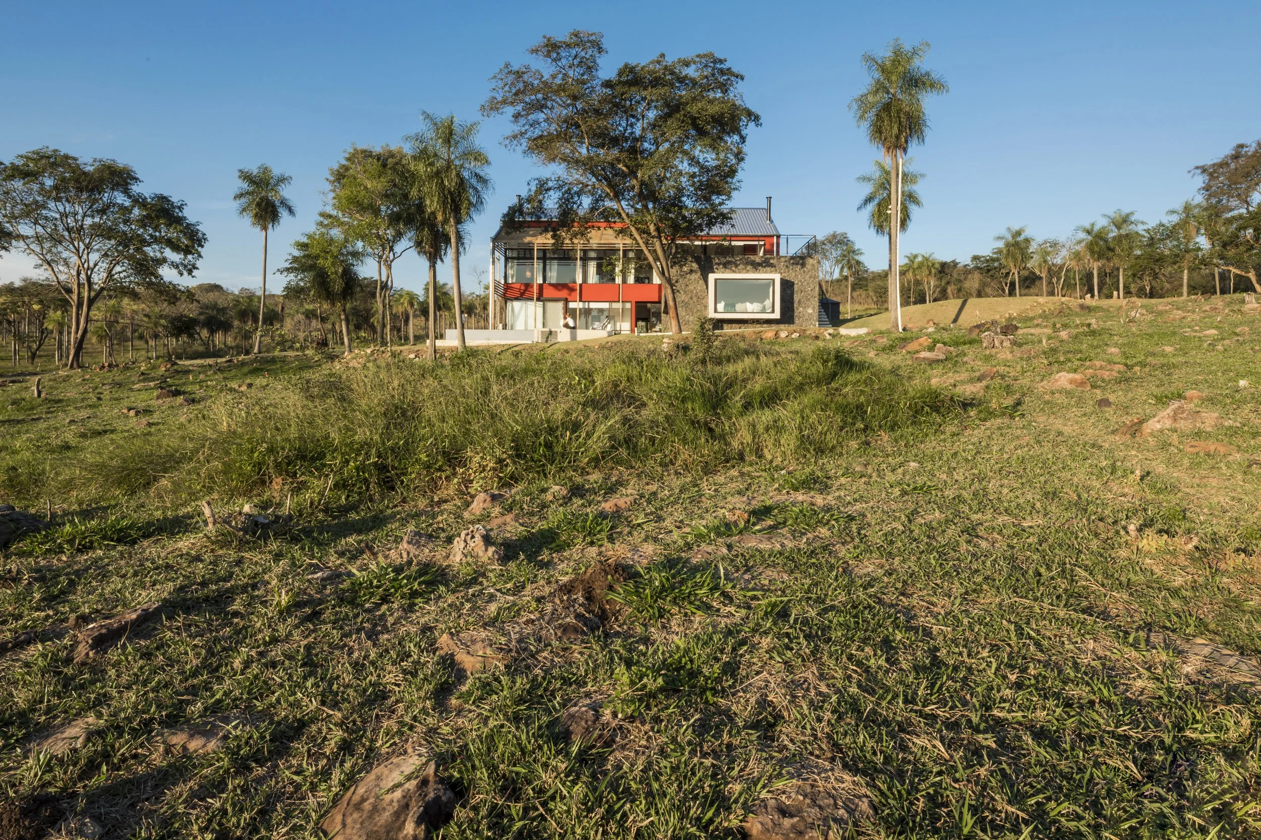 PRO ARQUITECTURA PARAGUAY architecture design PROSA
Casa moderna en medio de un paisaje de campo con árboles y césped, bajo un cielo despejado.