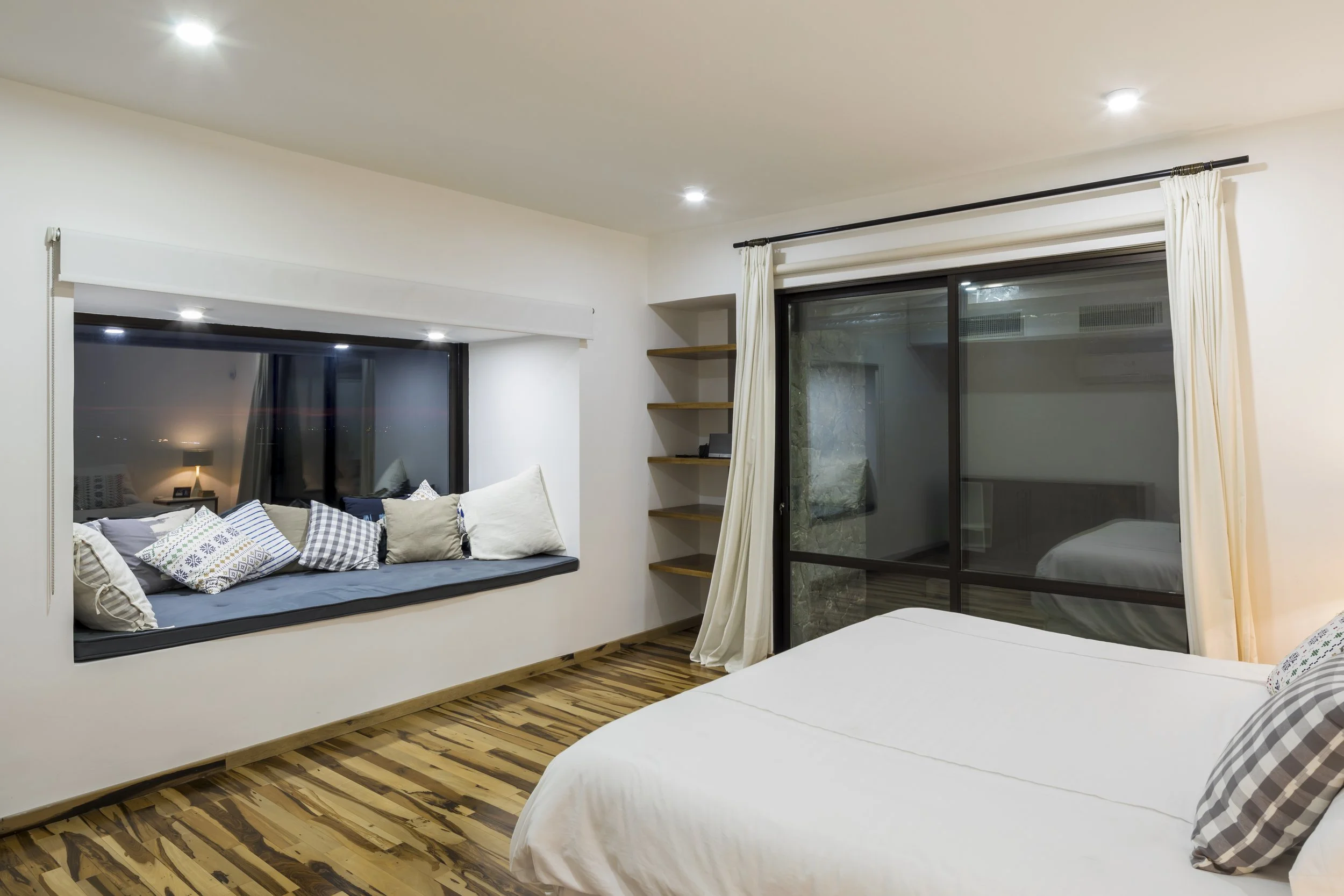PRO ARQUITECTURA PARAGUAY architecture design PROSA
Dormitorio con cama blanca, ventana grande con cortinas blancas, y área de descanso con cojines.