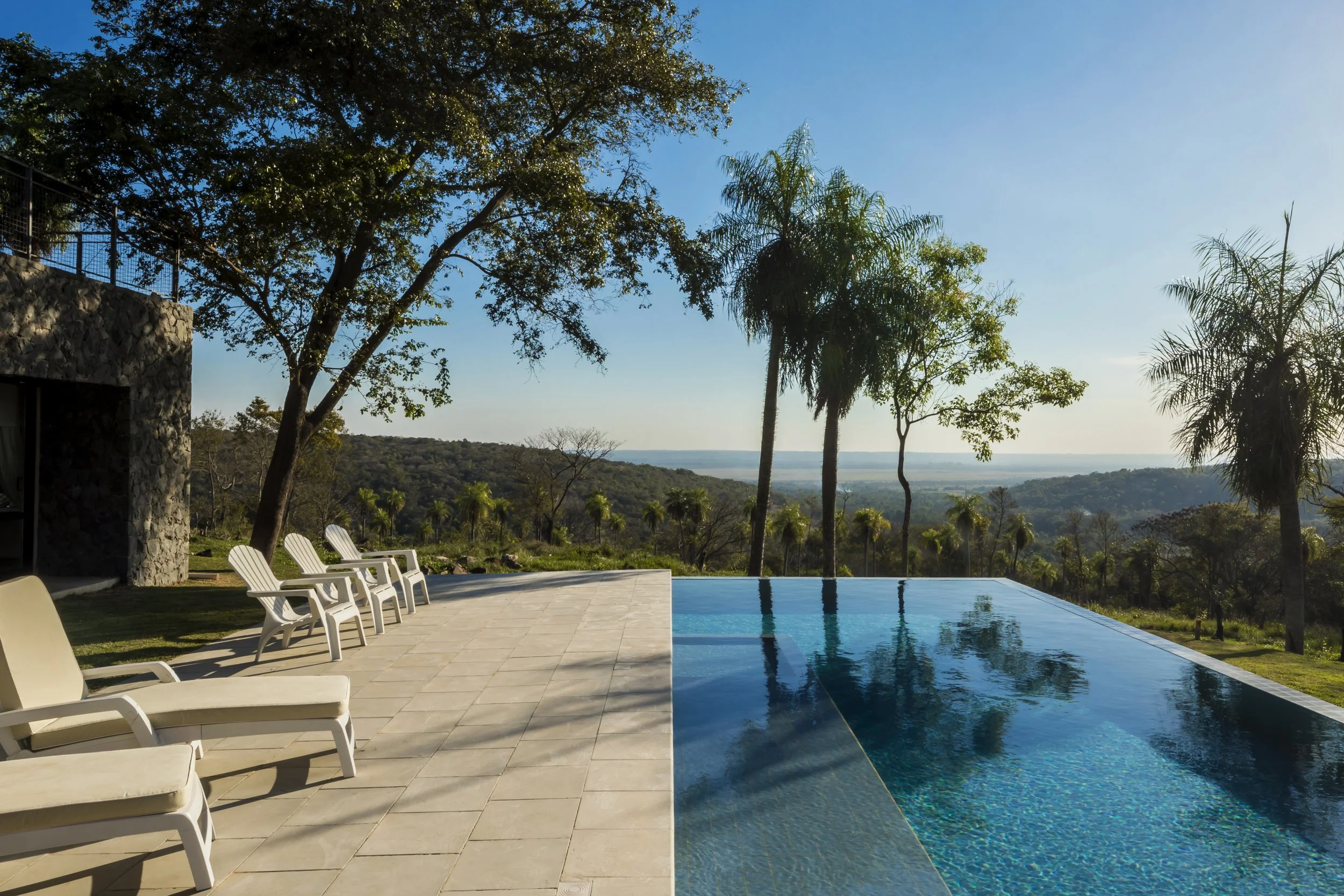 PRO ARQUITECTURA PARAGUAY architecture design PROSA
Piscina infinita al aire libre con sillas junto a árboles y vista panorámica de colinas y cielo despejado en fondo