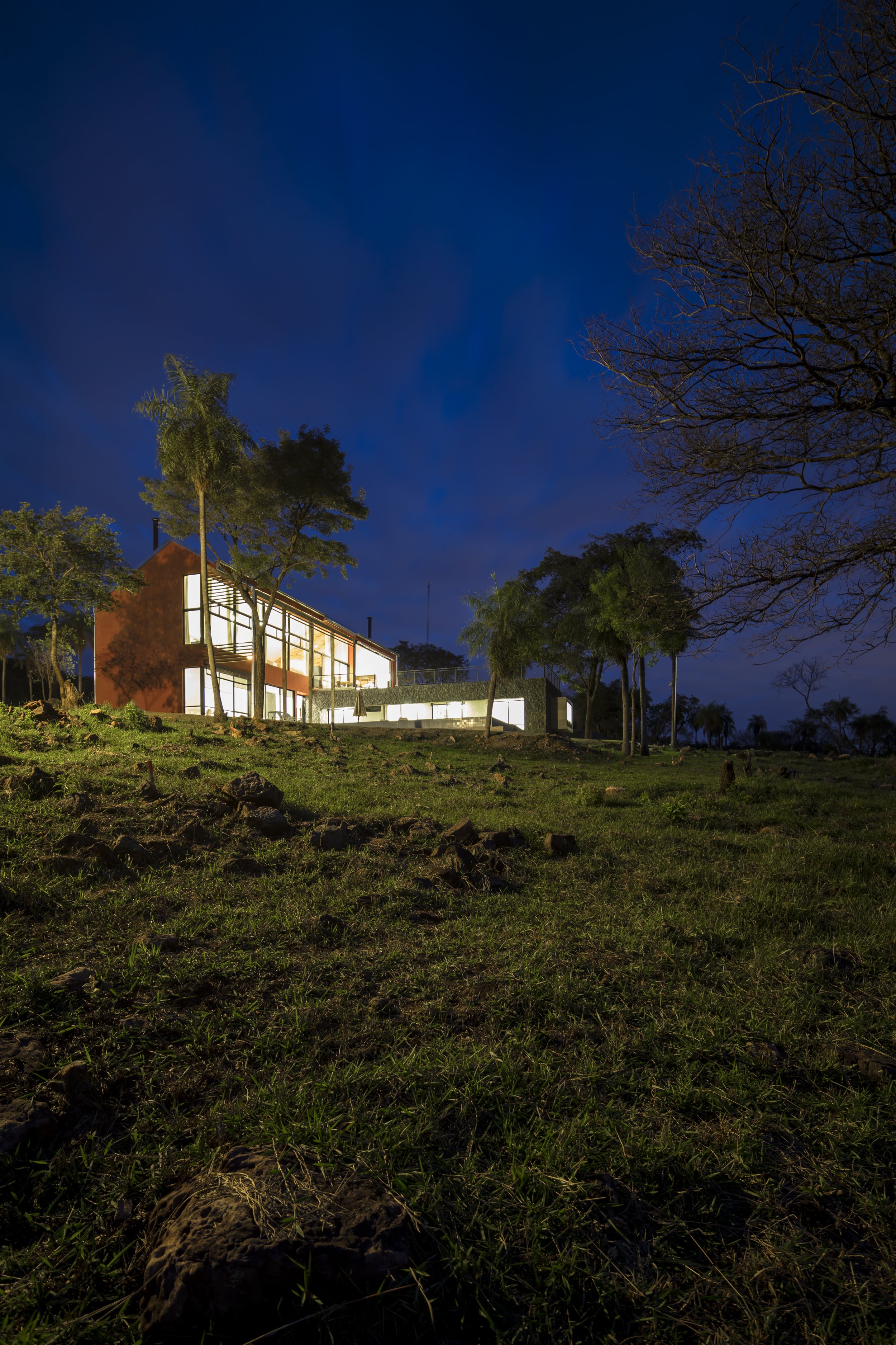 PRO ARQUITECTURA PARAGUAY architecture design PROSA
Casa moderna iluminada en un entorno natural durante la noche, con árboles y césped.