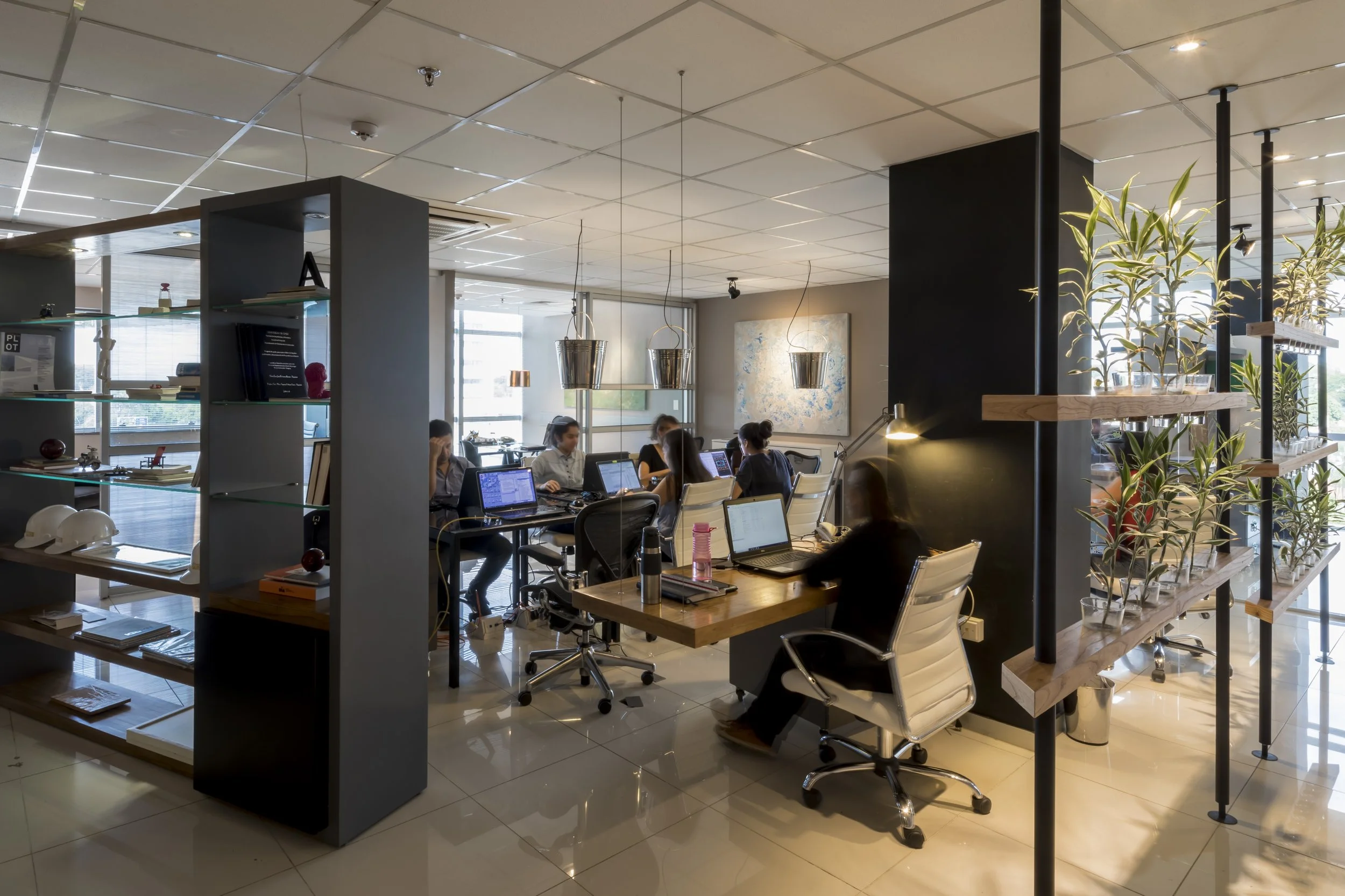 PRO ARQUITECTURA PARAGUAY architecture design PROSA
Oficina moderna con varias personas trabajando en escritorios con laptops, decorada con arte en la pared y plantas en estantes de madera, en un espacio abierto con luz natural.