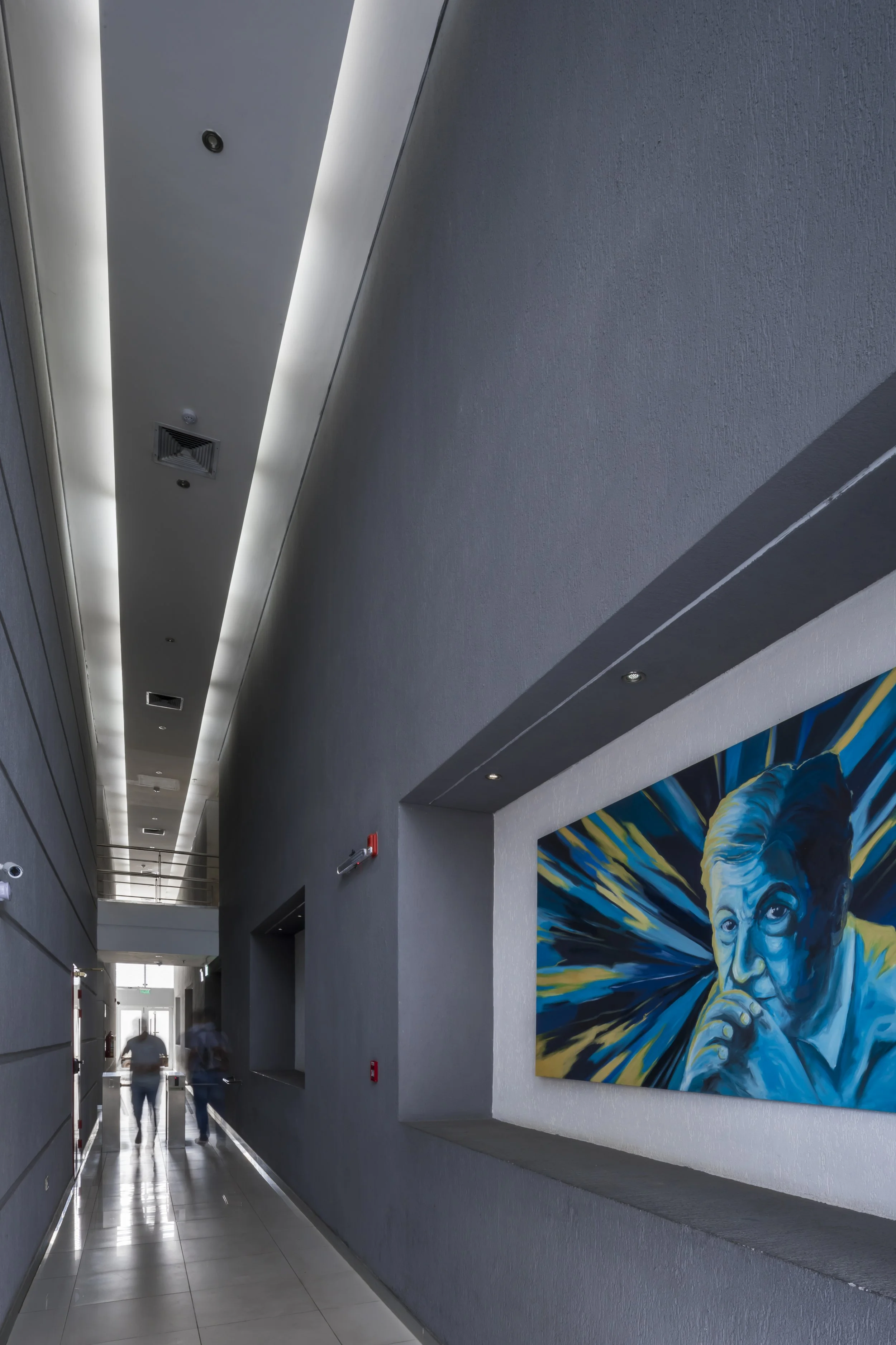 PRO ARQUITECTURA PARAGUAY architecture design PROSA
Pasillo moderno con paredes grises, techo con iluminación empotrada y una pintura de un retrato de color azul en la pared derecha.