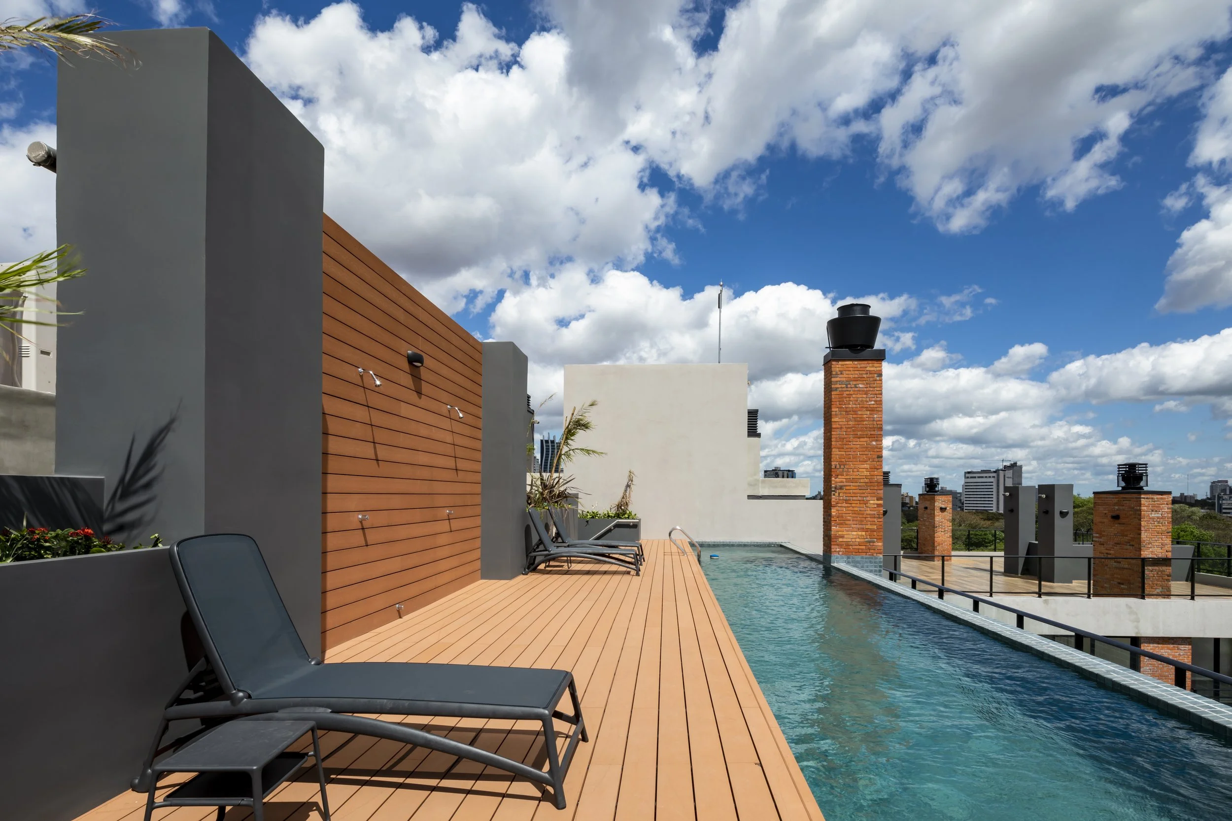 Terraza en la azotea con piscina, sillas y vista urbana, cielo despejado con nubes blancas.