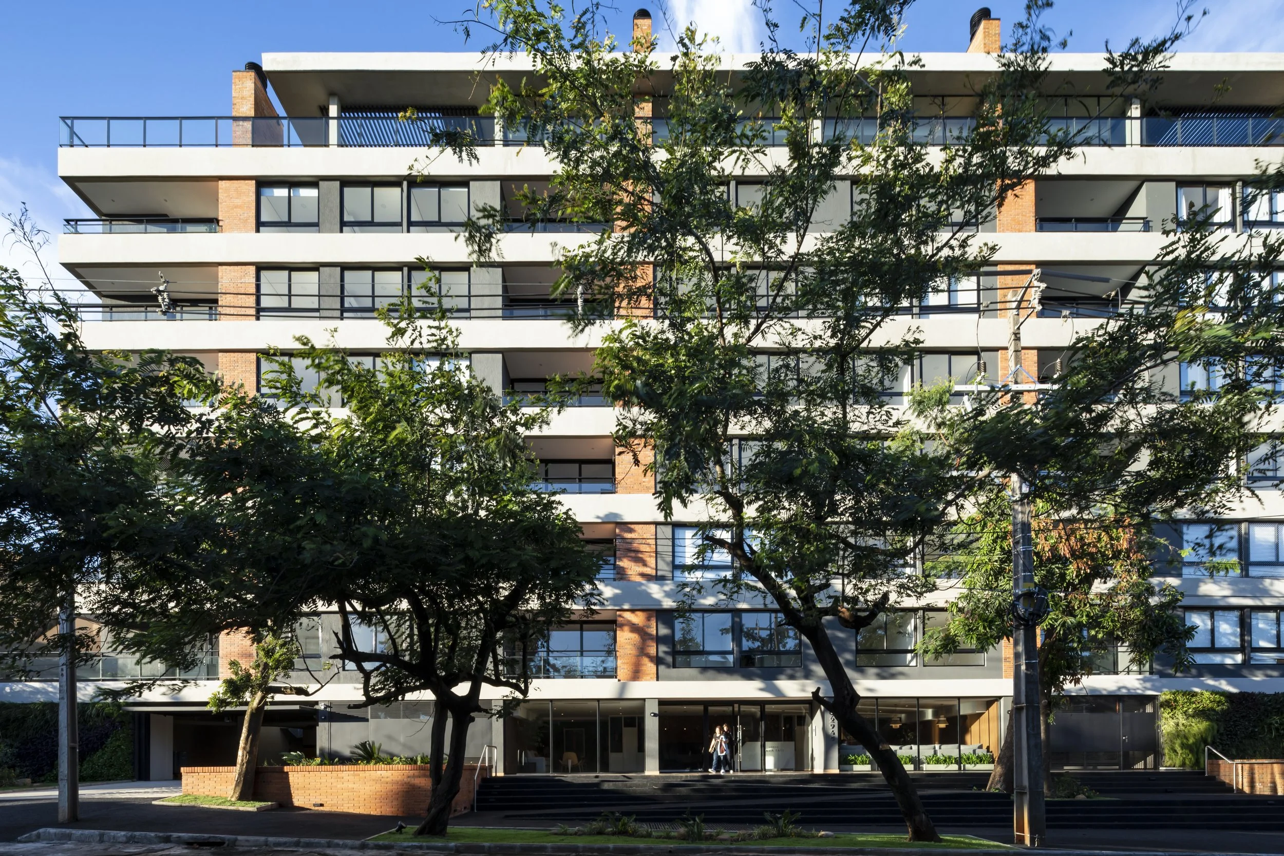 Edificio de apartamentos moderno con varias plantas, árboles en primer plano y ventanas grandes.