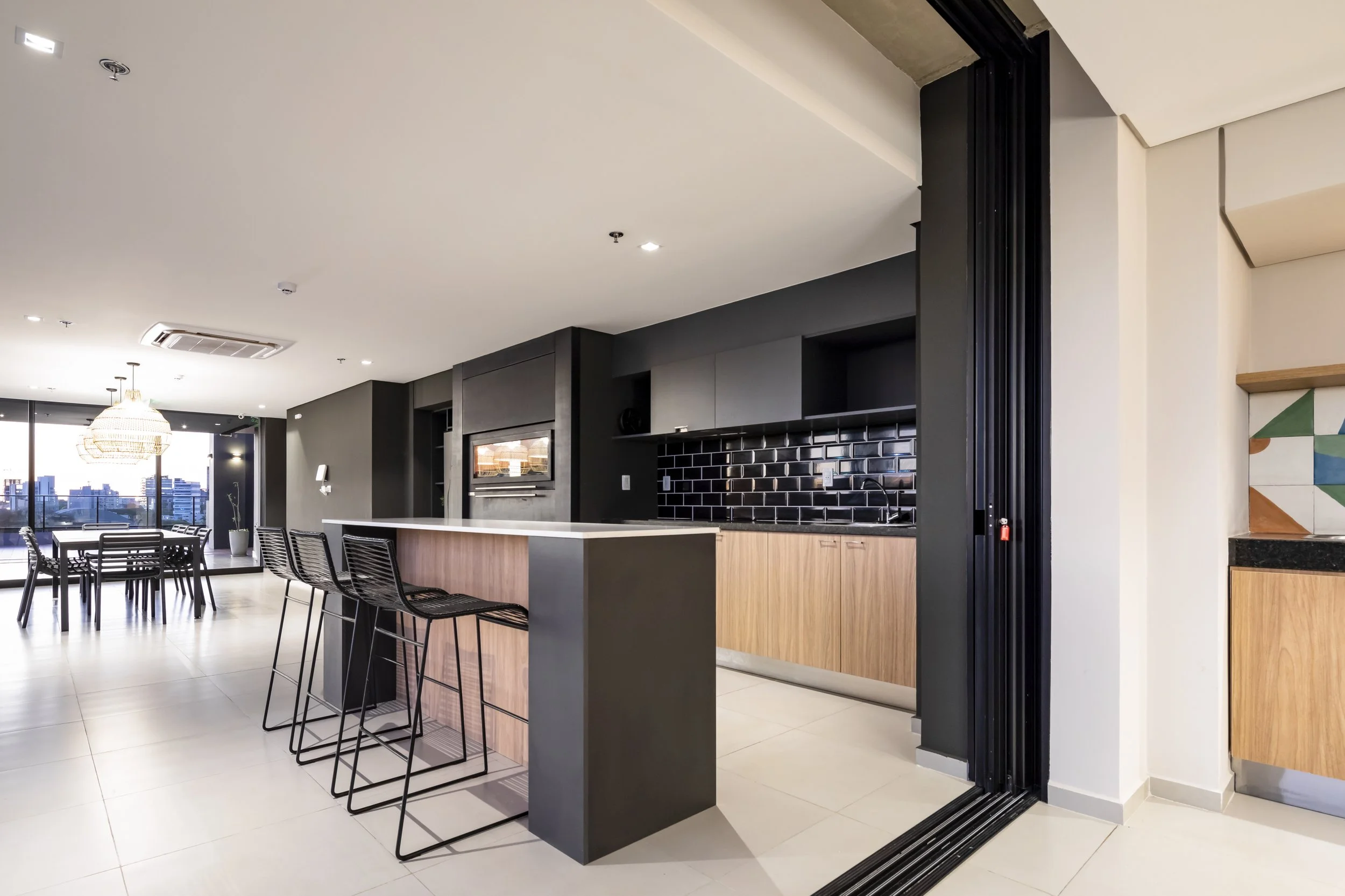 Interior moderno de apartamento, con área de cocina y comedor con vista a la ciudad, muebles de madera y sillas negras.