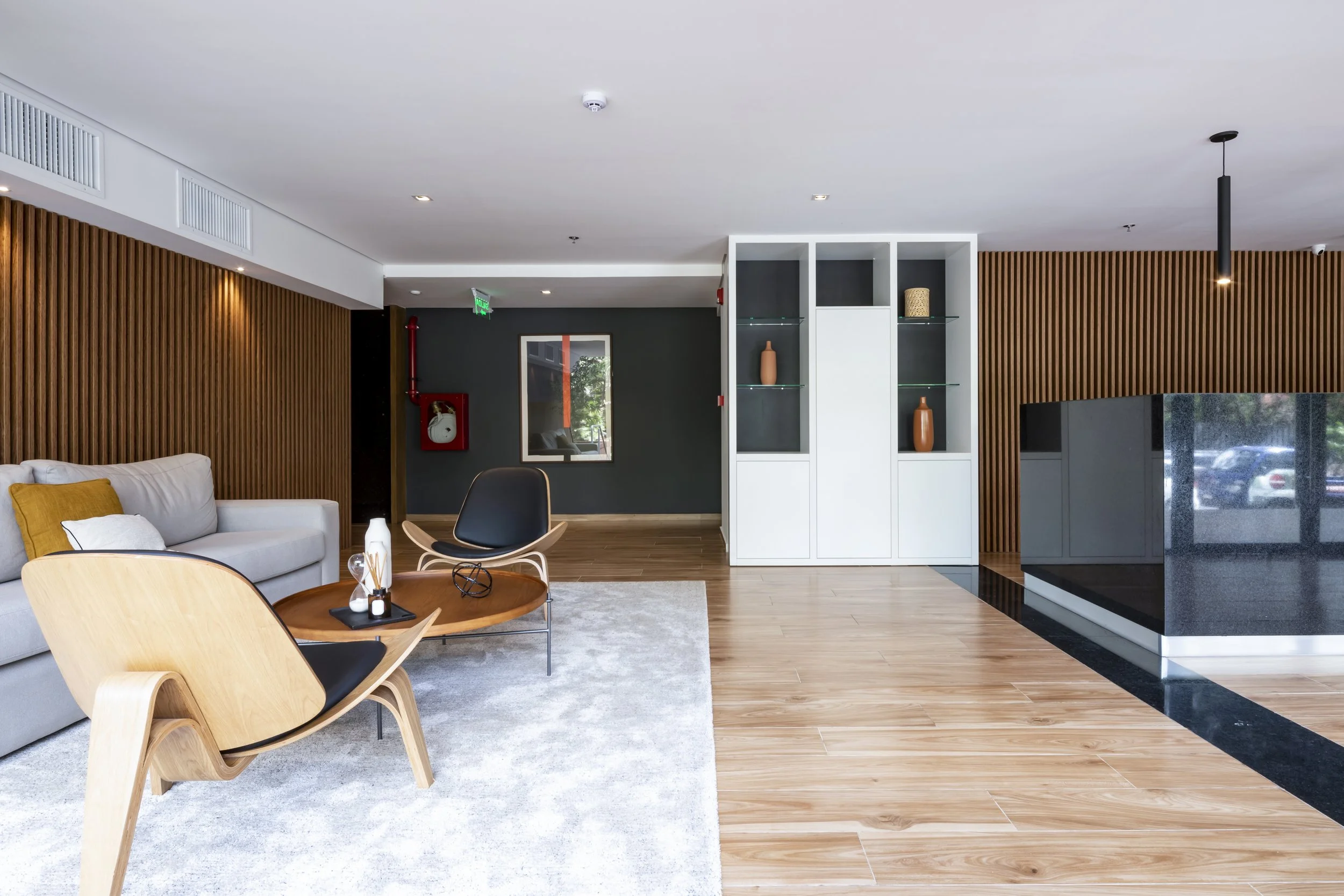 Sala moderna con sofá gris, sillón de madera y asiento negro, mesa de centro de madera, pared de madera, guardarropa blanco con decoración en baldosas negras y jarrones