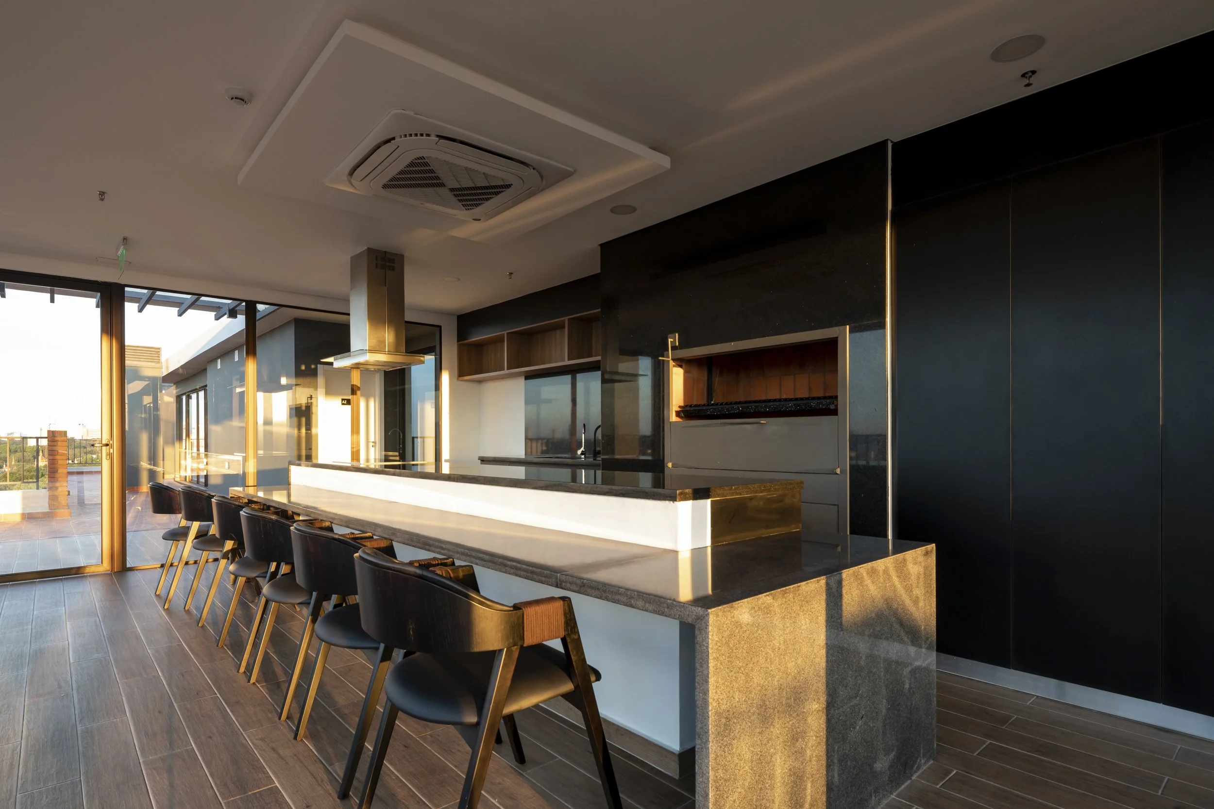 	
PRO ARQUITECTURA PARAGUAY architecture design PROSA
Una cocina moderna con barra de granito y seis sillones negros, ventanas grandes con vista al exterior y ventiladores en el techo.