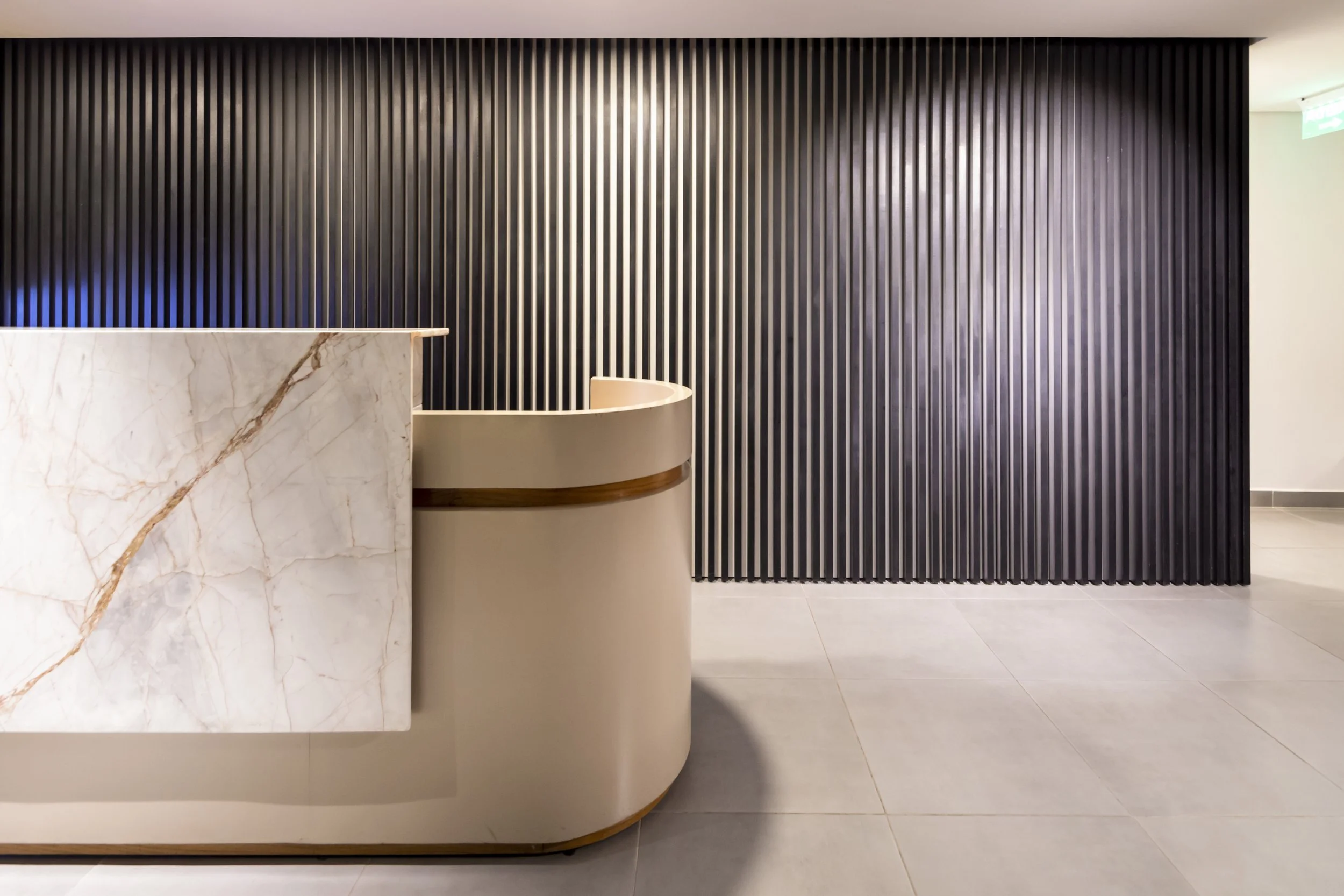 	
PRO ARQUITECTURA PARAGUAY architecture design PROSA
Área de recepción moderna con mostrador de mármol blanco y pared de paneles de madera en tonos oscuros.