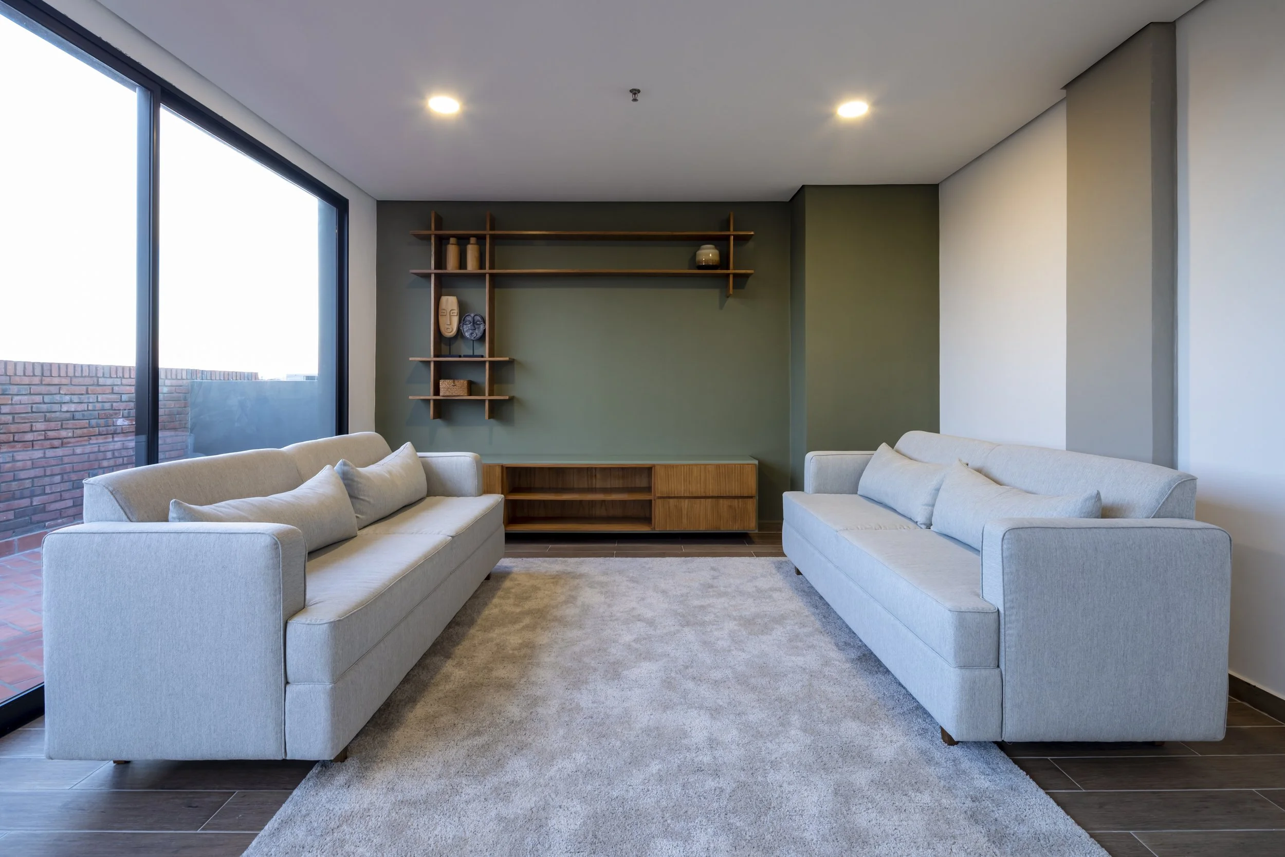 	
PRO ARQUITECTURA PARAGUAY architecture design PROSA
Sala de estar con dos sillones blancos, un mueble de madera, estantería con decoración y artefactos en pared verde, ventana grande con vista a balcón de ladrillos.