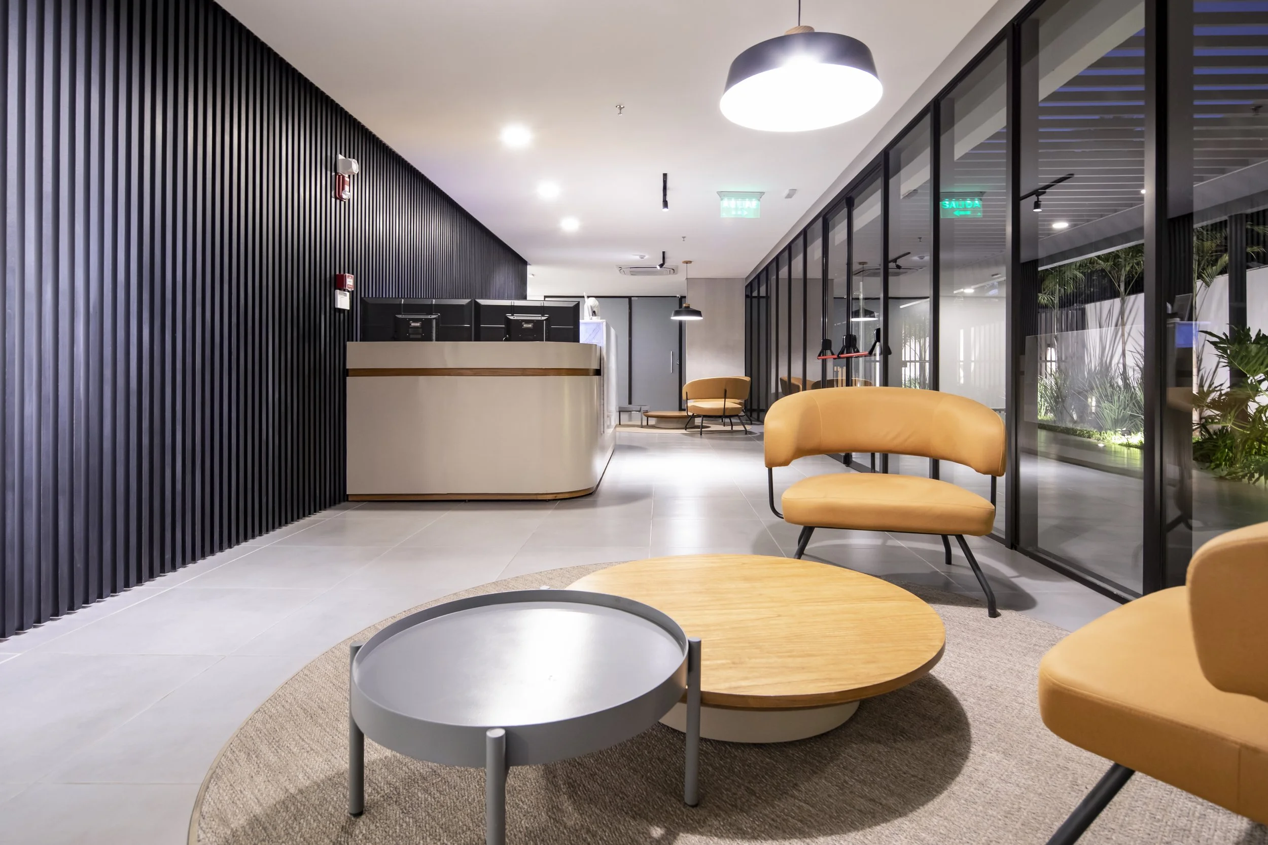 	
PRO ARQUITECTURA PARAGUAY architecture design PROSA
Vestíbulo de un edificio moderno con sillones beige, mesas de madera y decoración minimalista, con paredes de cristal y planta al fondo.