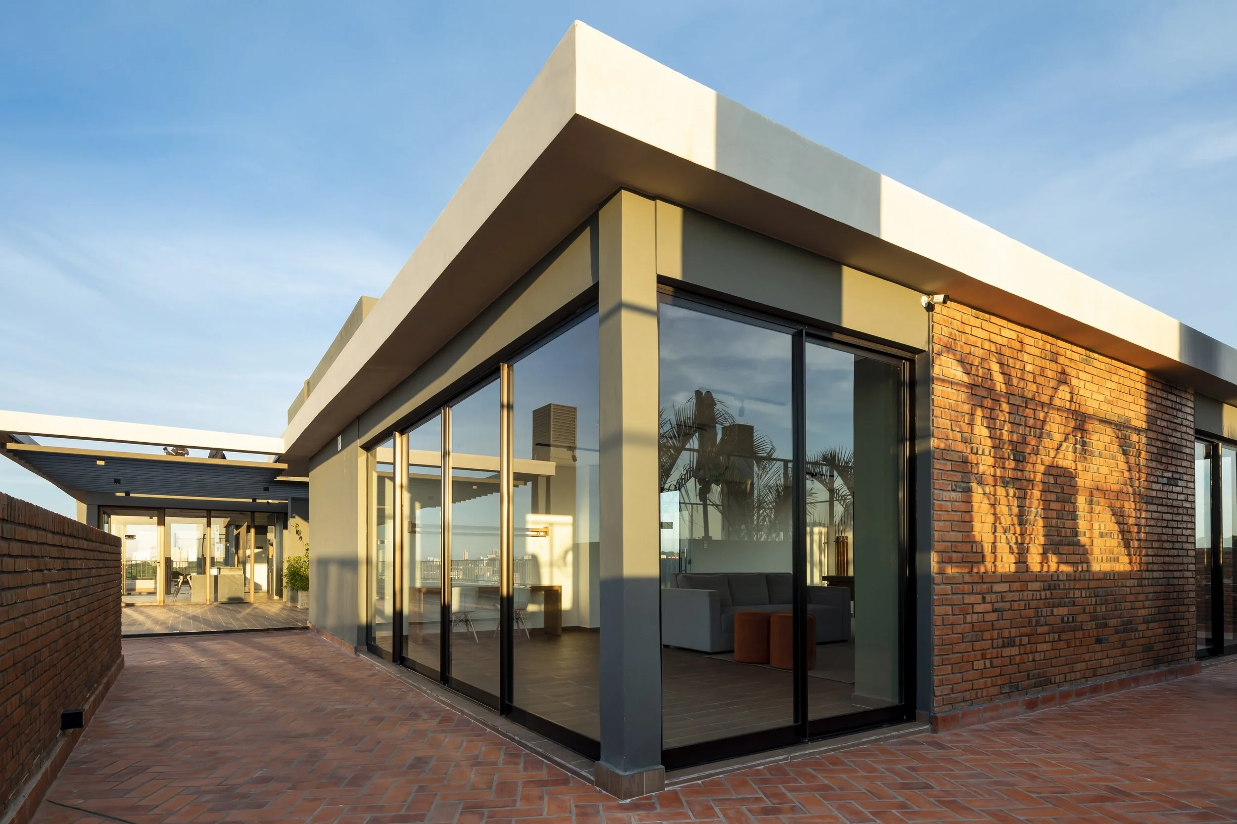 	
PRO ARQUITECTURA PARAGUAY architecture design PROSA
Vista exterior de una moderna casa con paredes de ladrillo y grandes ventanas de vidrio, en un atardecer con cielo despejado.