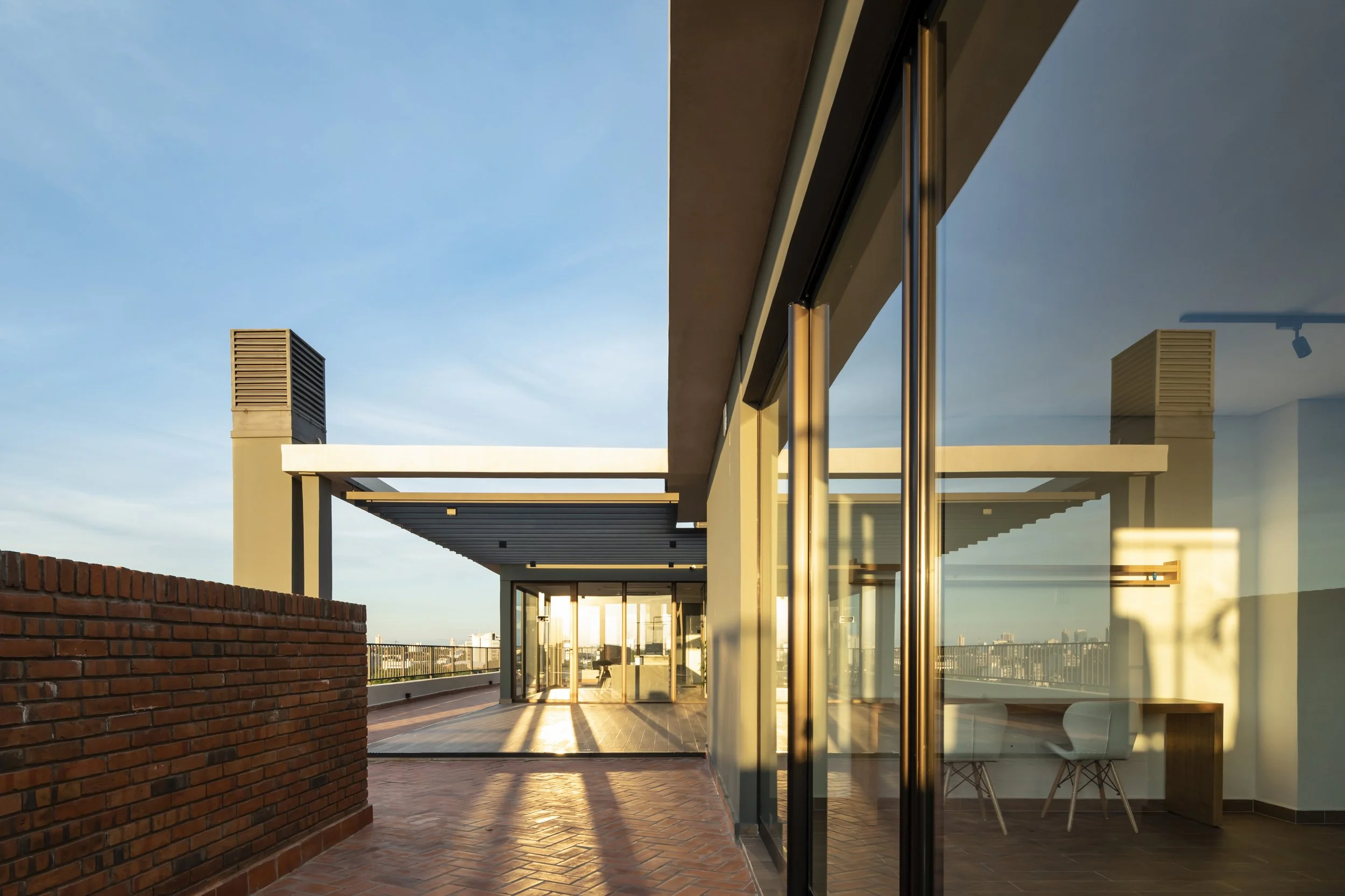 	
PRO ARQUITECTURA PARAGUAY architecture design PROSA
Vista de un techo moderno con paredes de cristal y una terraza con ladrillos, durante el atardecer, en una ciudad.