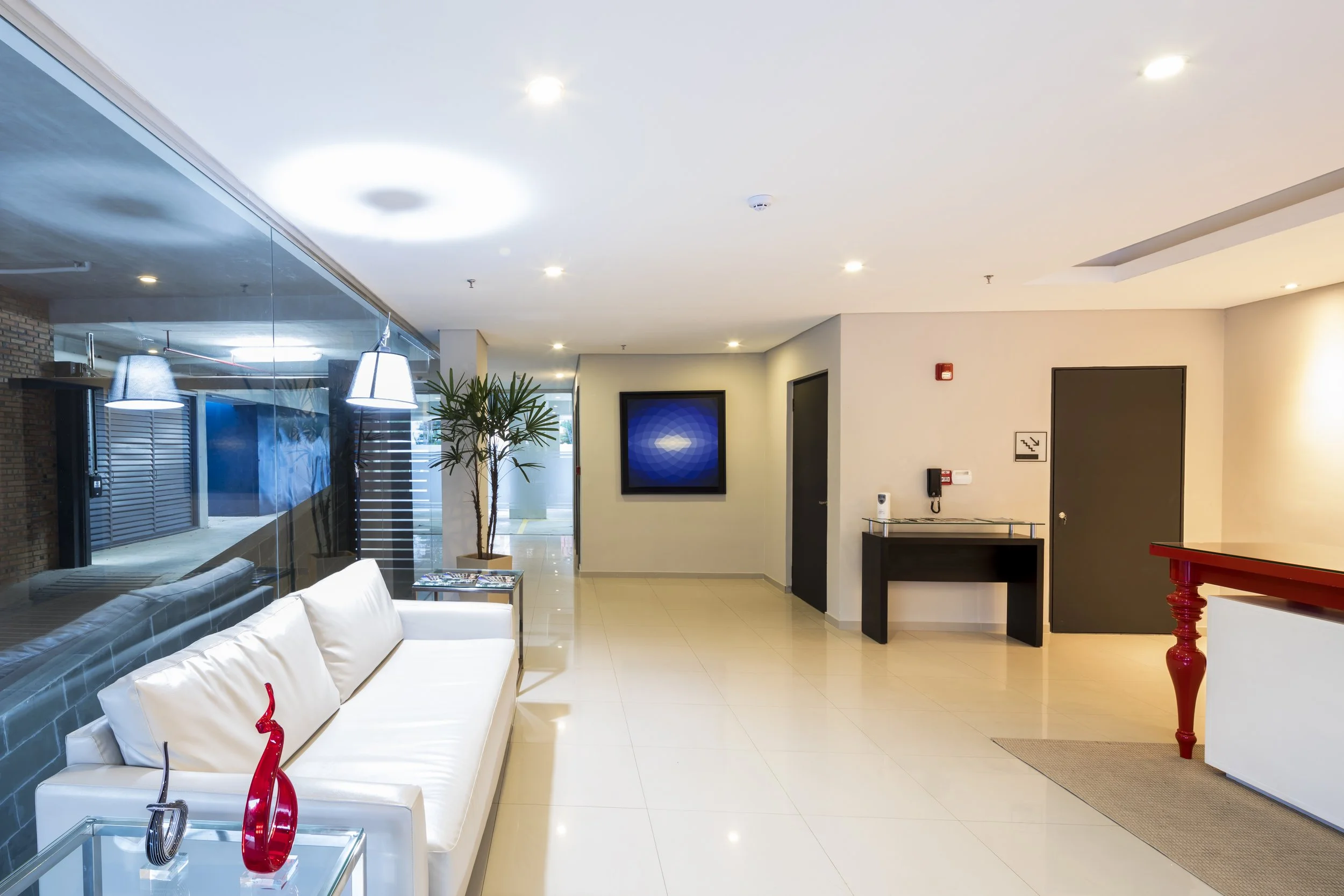 	
PRO ARQUITECTURA PARAGUAY architecture design PROSA
Vestíbulo de hotel con sofá blanco, lámparas, planta decorativa, mesa con objetos, paredes blancas, puertas negras y TV de pantalla plana.