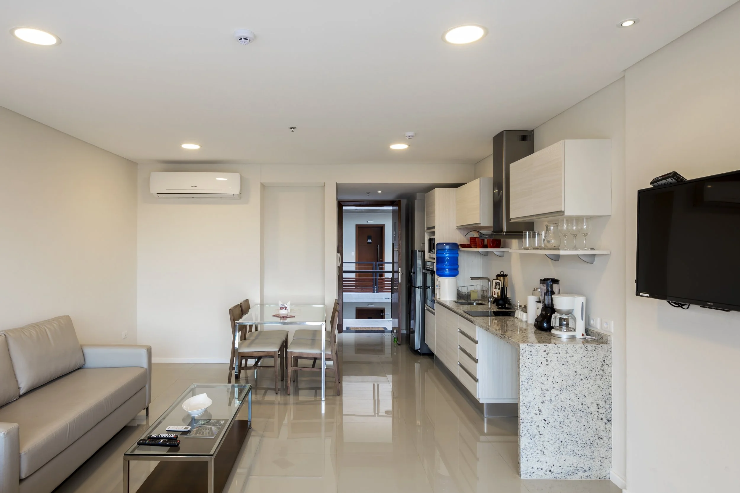 	
PRO ARQUITECTURA PARAGUAY architecture design PROSA
Sala de estar y cocina en un apartamento, con sofá beige, mesa de cristal, comedor, electrodomésticos y televisor.