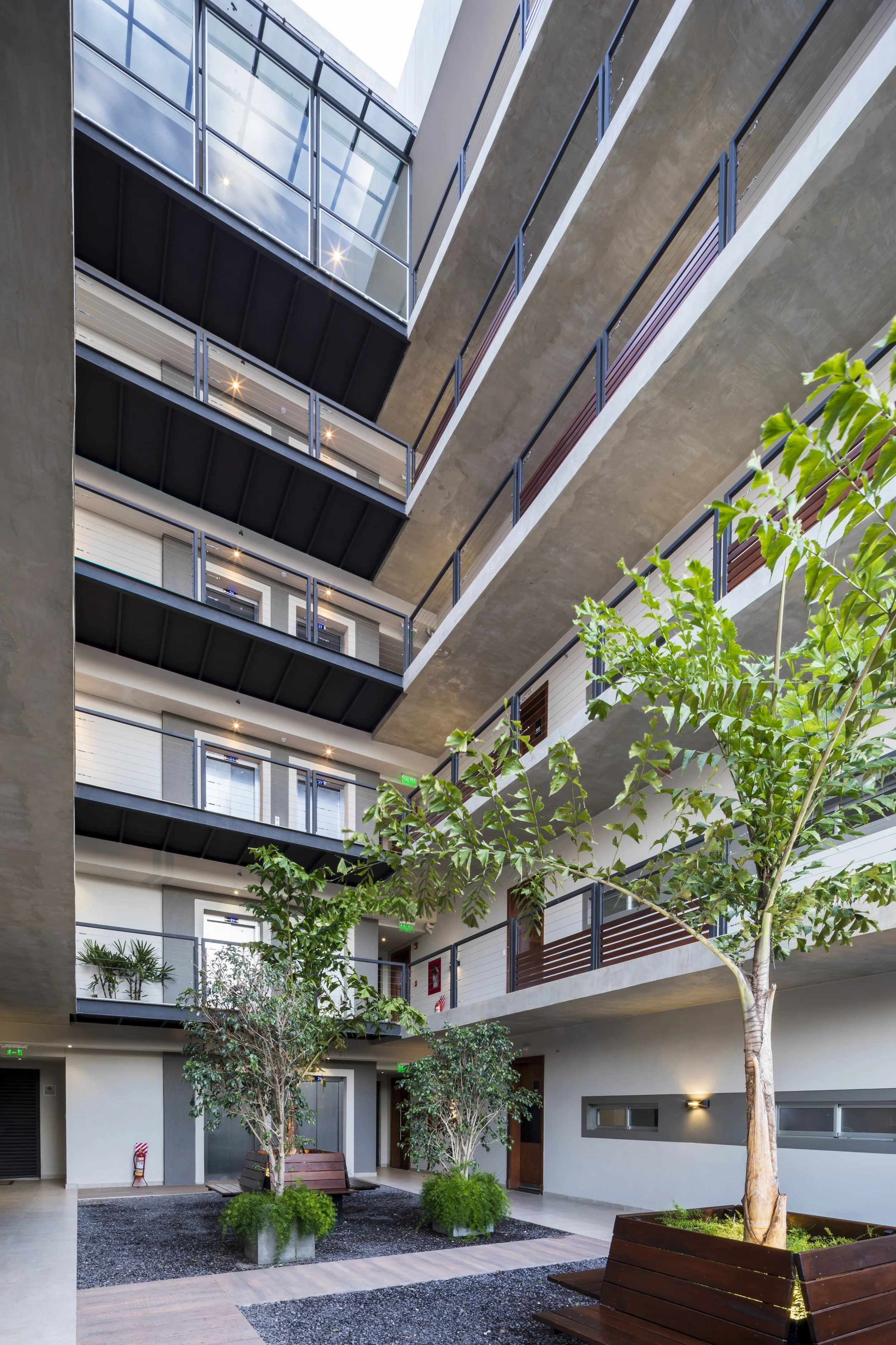 	
PRO ARQUITECTURA PARAGUAY architecture design PROSA
Interior de un edificio con jardín central, plantas, árboles en macetas de madera, pasillos en cada piso, barandillas de metal, ventanas y luces en los techos.