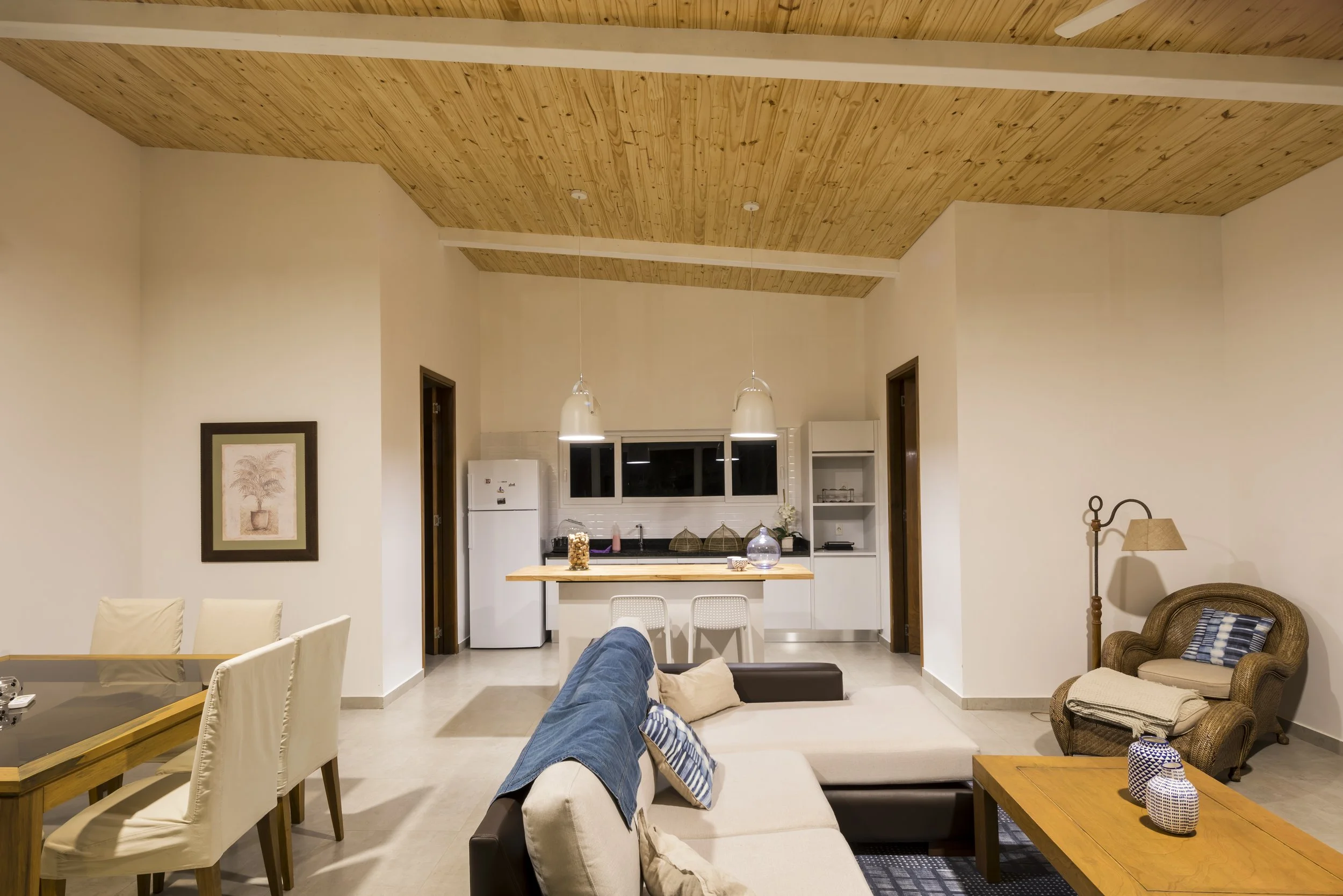 	
PRO ARQUITECTURA PARAGUAY architecture design PROSA
Sala de estar con comedor y cocina en fondo, sillones, lámparas, cuadros y decoración en colores neutros y madera.