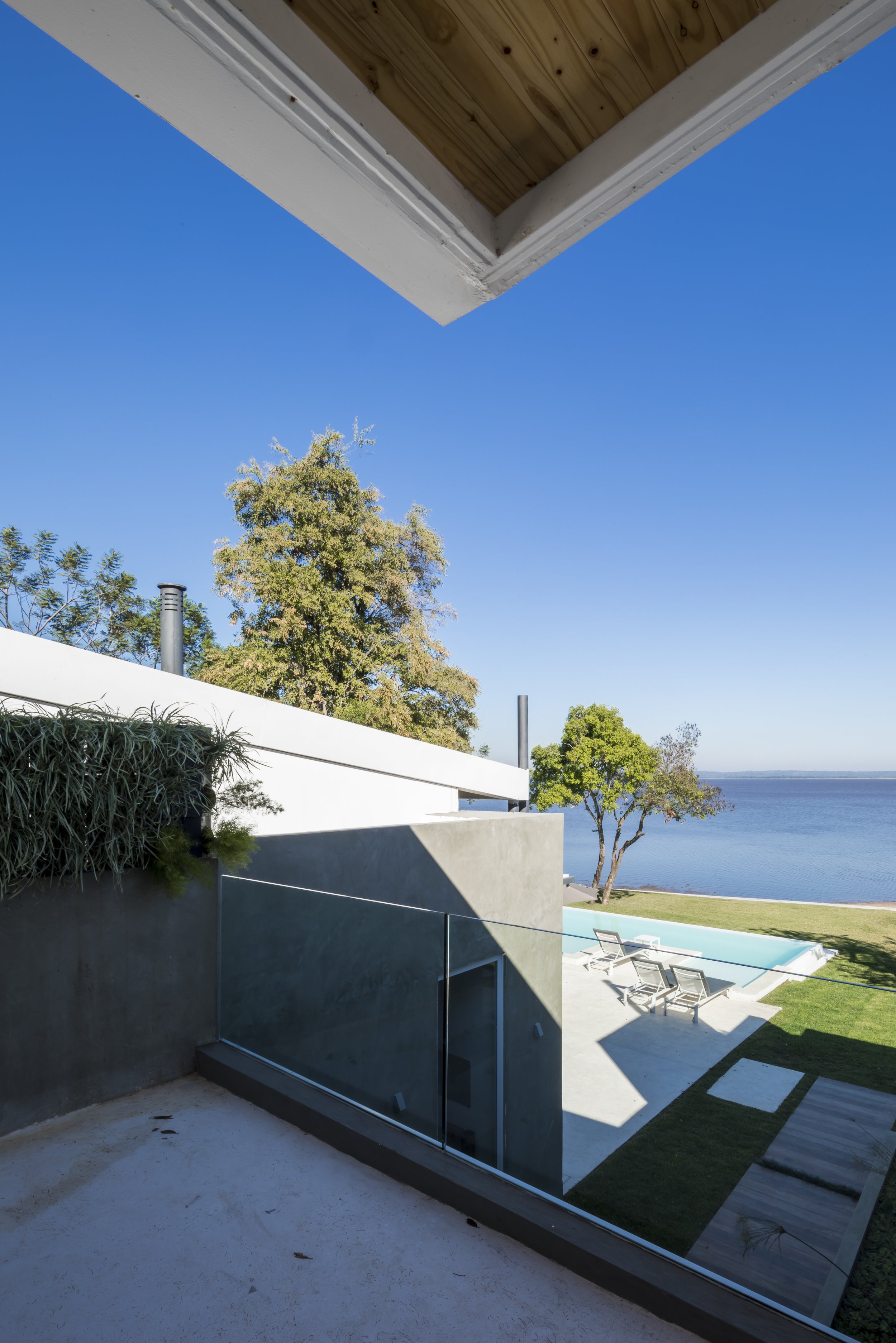 Vista del patio con piscina y vista al lago, con varias tumbonas y árboles verdes bajo un cielo azul claro