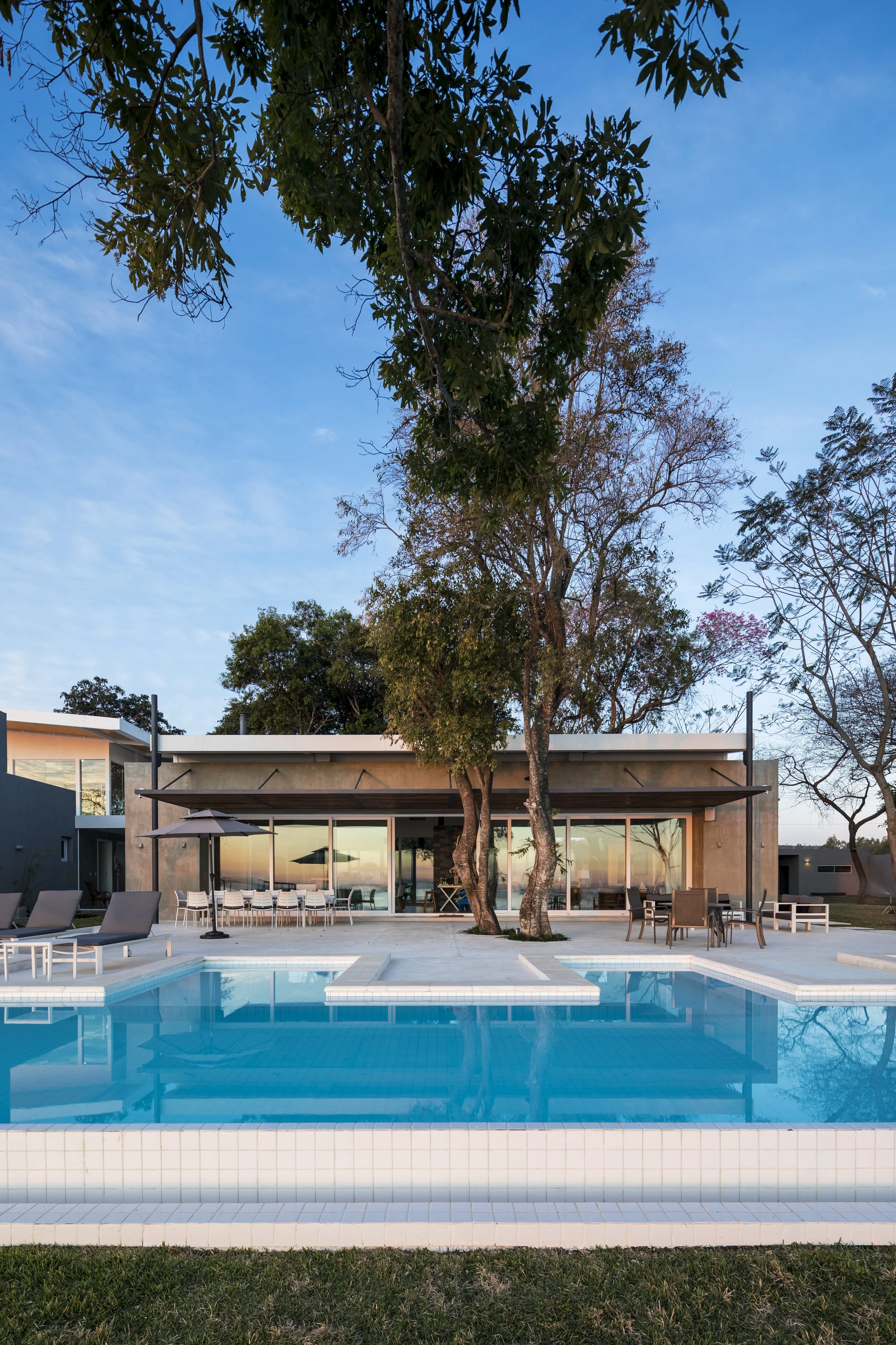 	
PRO ARQUITECTURA PARAGUAY architecture design PROSA
Piscina lado exterior de una casa moderna con árboles y muebles de patio, durante el atardecer.