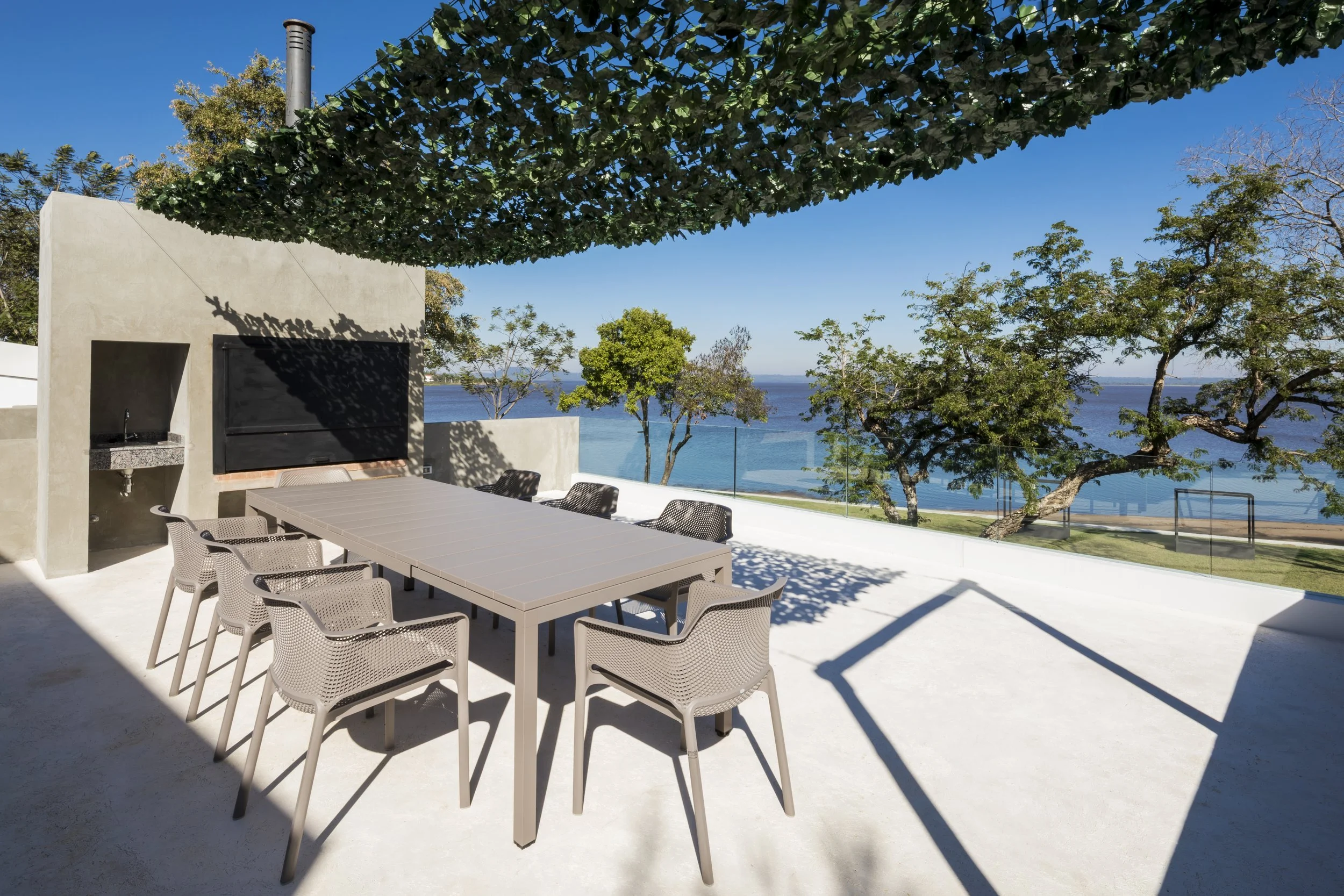 	
PRO ARQUITECTURA PARAGUAY architecture design PROSA
Terraza con mesa de comedor y sillas, vista al río con árboles y cielo despejado.