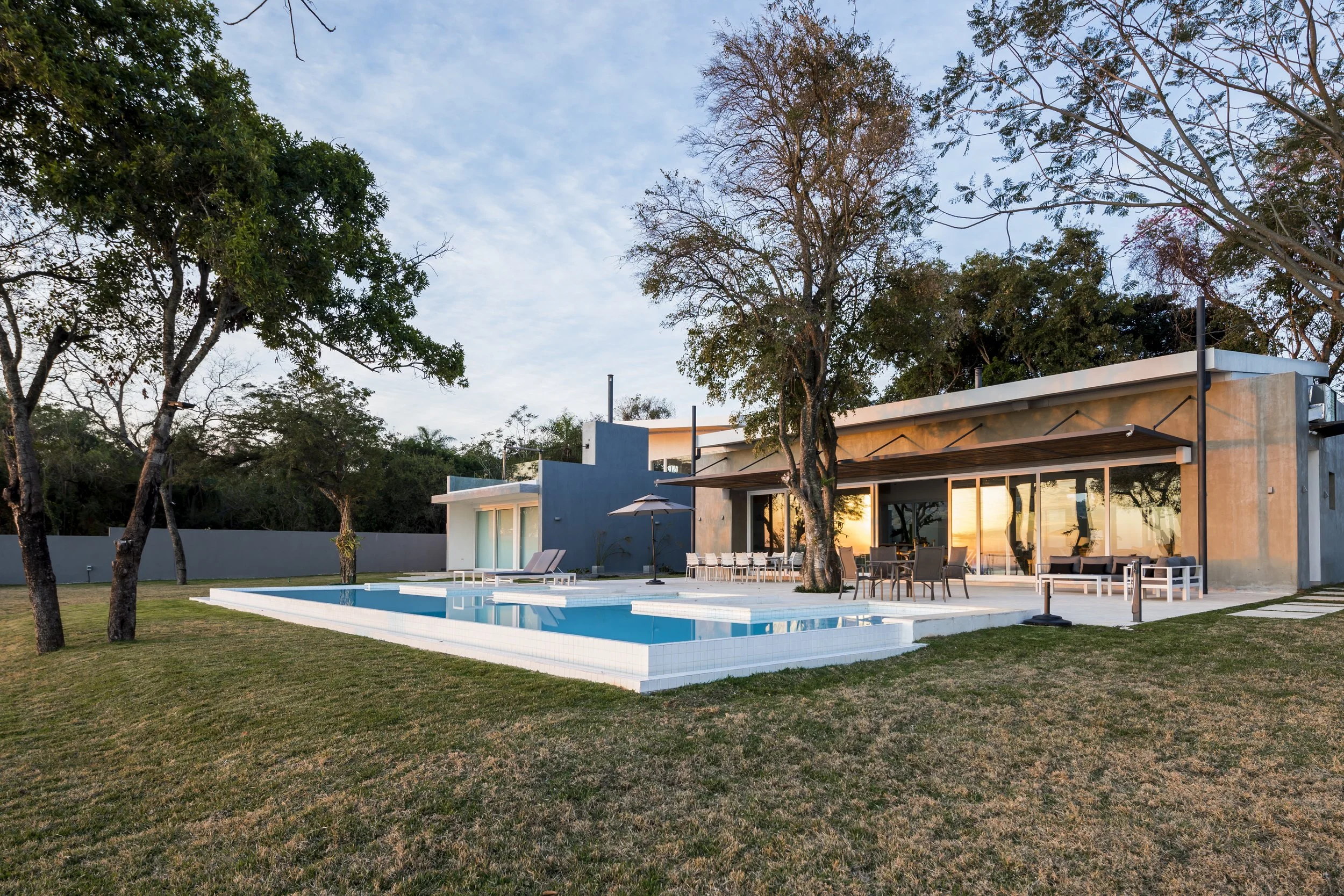 	
PRO ARQUITECTURA PARAGUAY architecture design PROSA
Casa moderna con piscina y área de descanso en el jardín al atardecer