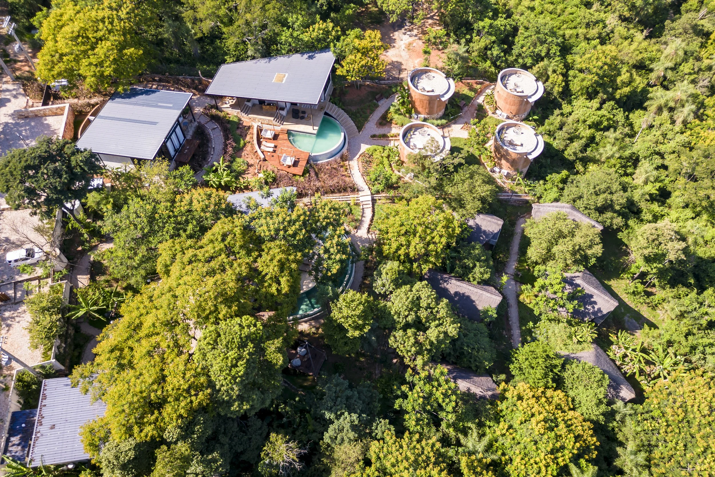 Vista aérea de un complejo de cabañas rodeadas de árboles, con varias estructuras, caminos y una piscina en medio.