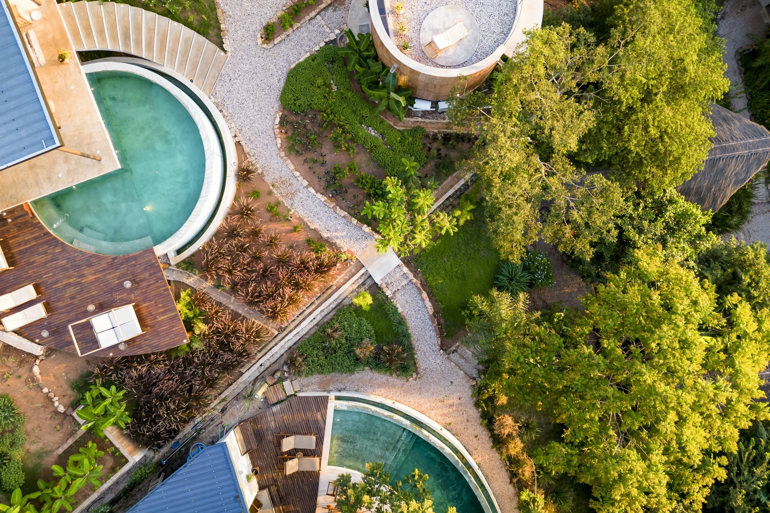 Vista aérea de piscinas en un jardín con césped, árboles grandes y senderos de piedra.