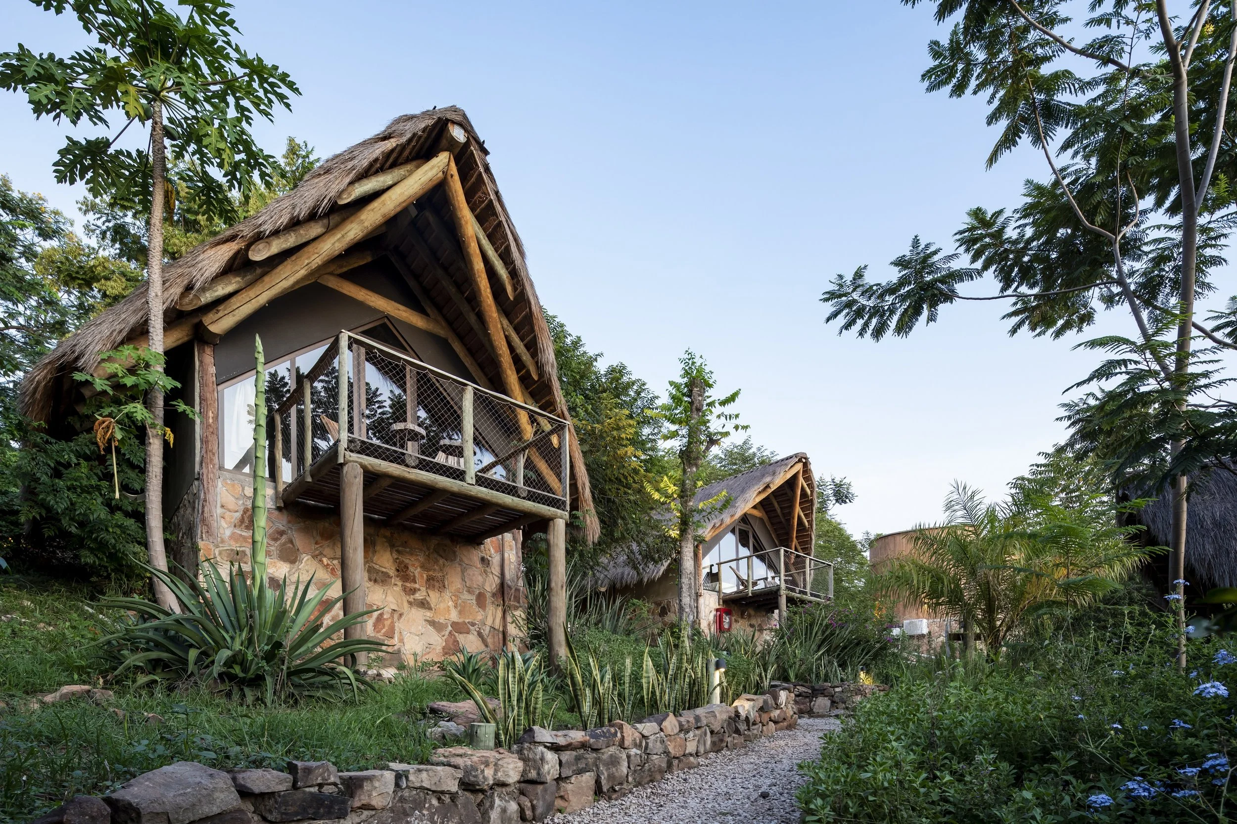 PRO ARQUITECTURA PARAGUAY arquitectos design architecture PROSA Casas de estilo rústico en un entorno natural con muchas plantas y árboles, en un día despejado.