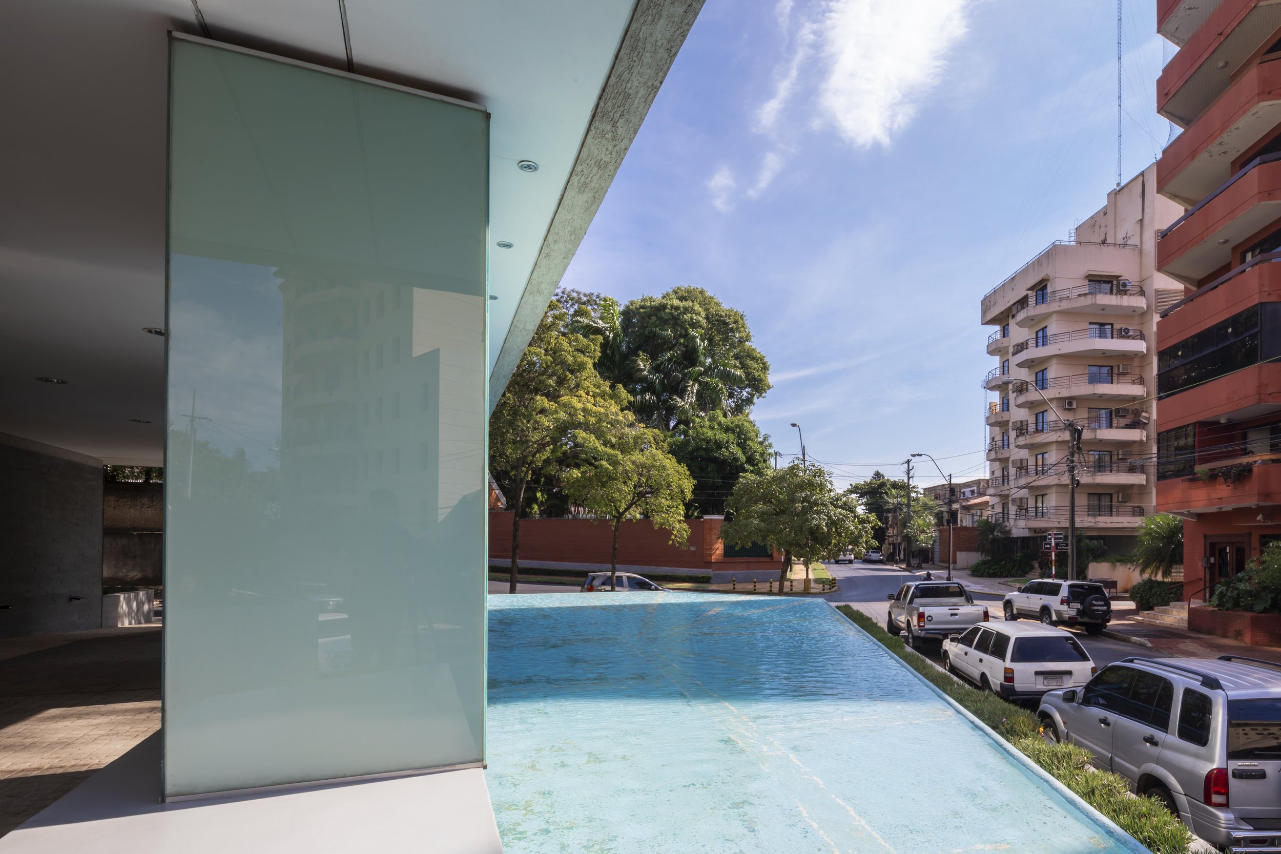 Vista de una piscina y calles urbanas con árboles y edificios en un día soleado.