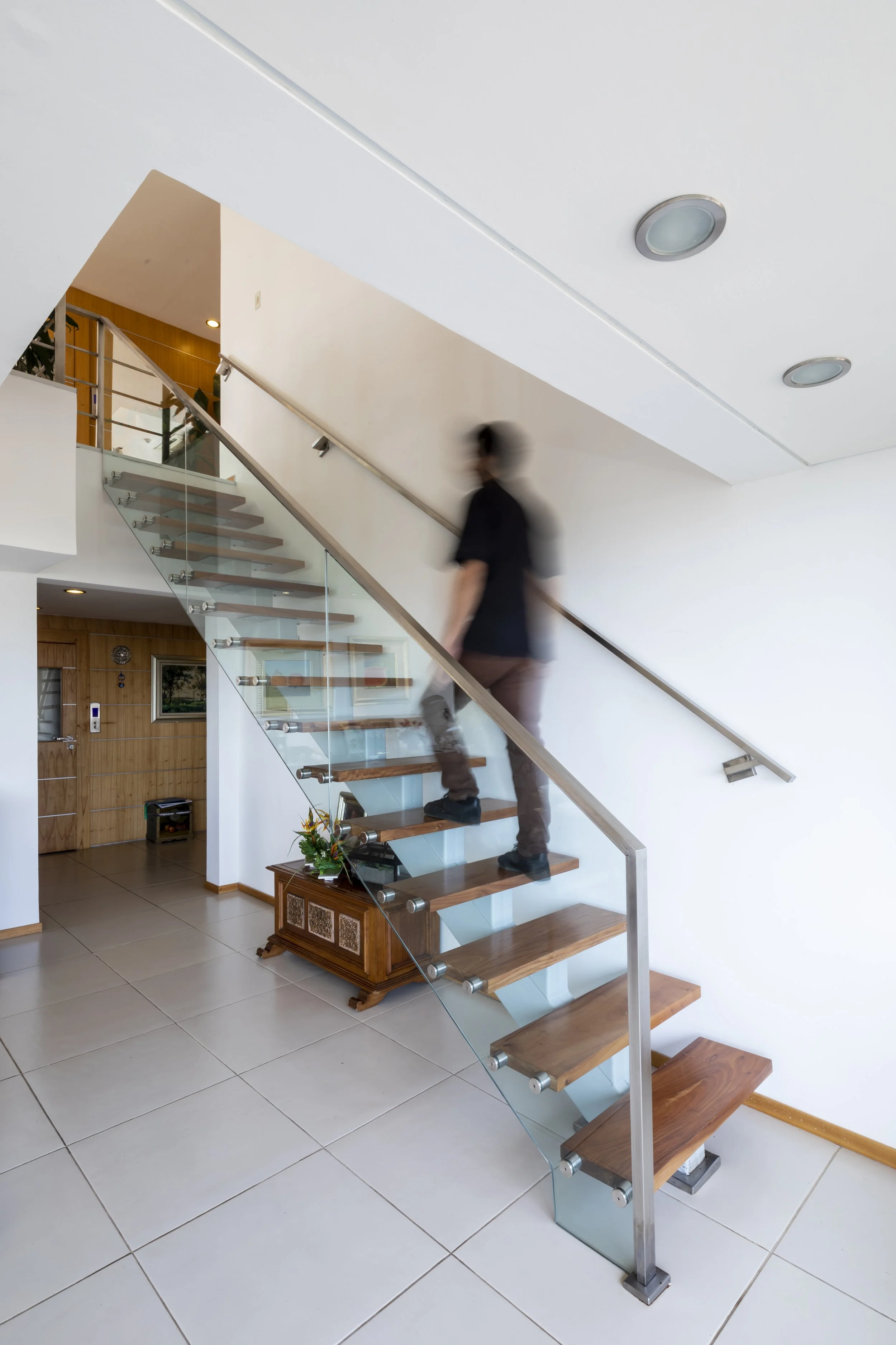 Una persona subiendo por una escalera moderna de madera y vidrio en el interior de una casa.