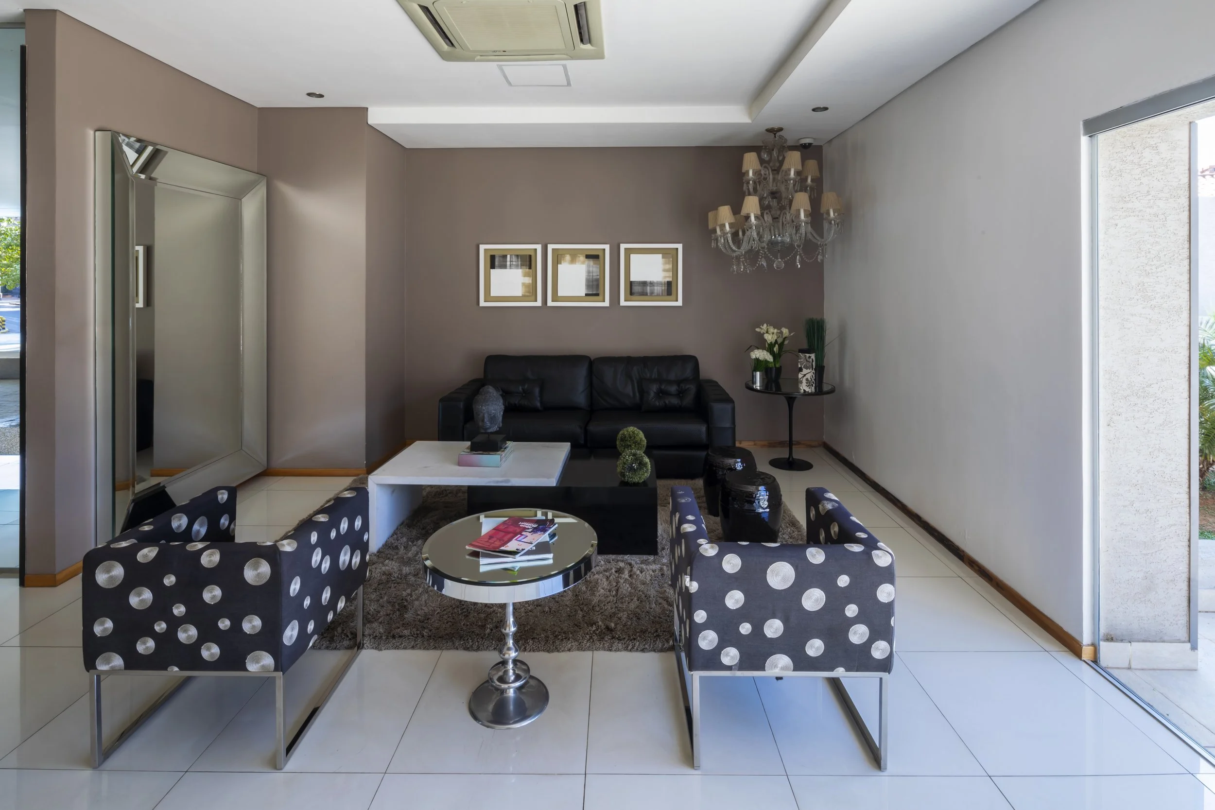 Sala de estar moderna con sillones de color negro, mesa blanca y complementos decorativos, como cuadros y plantas.