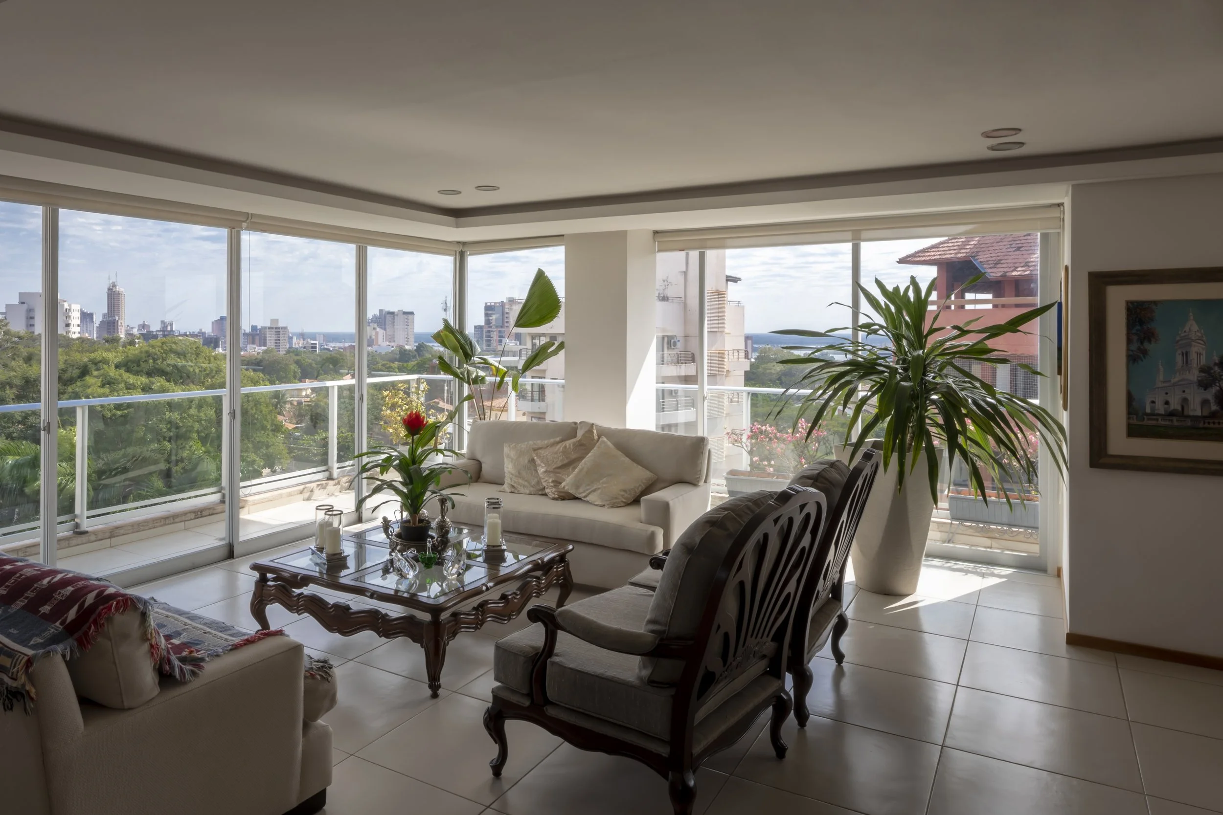 Sala de estar con vista panorámica a la ciudad, plantas grandes y muebles elegantes.