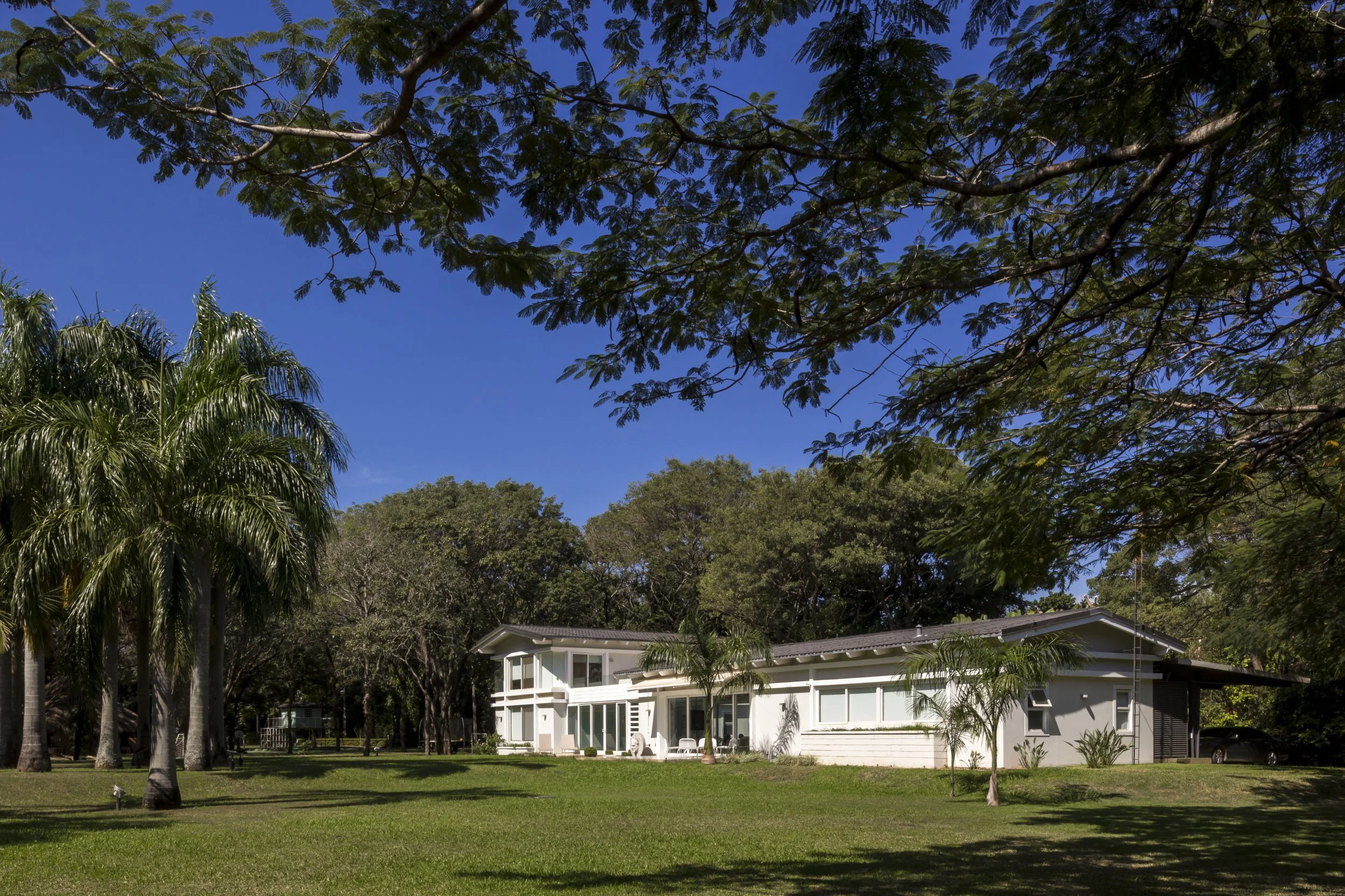 Casa moderna blanca rodeada de árboles y césped en un día soleado con cielo azul.