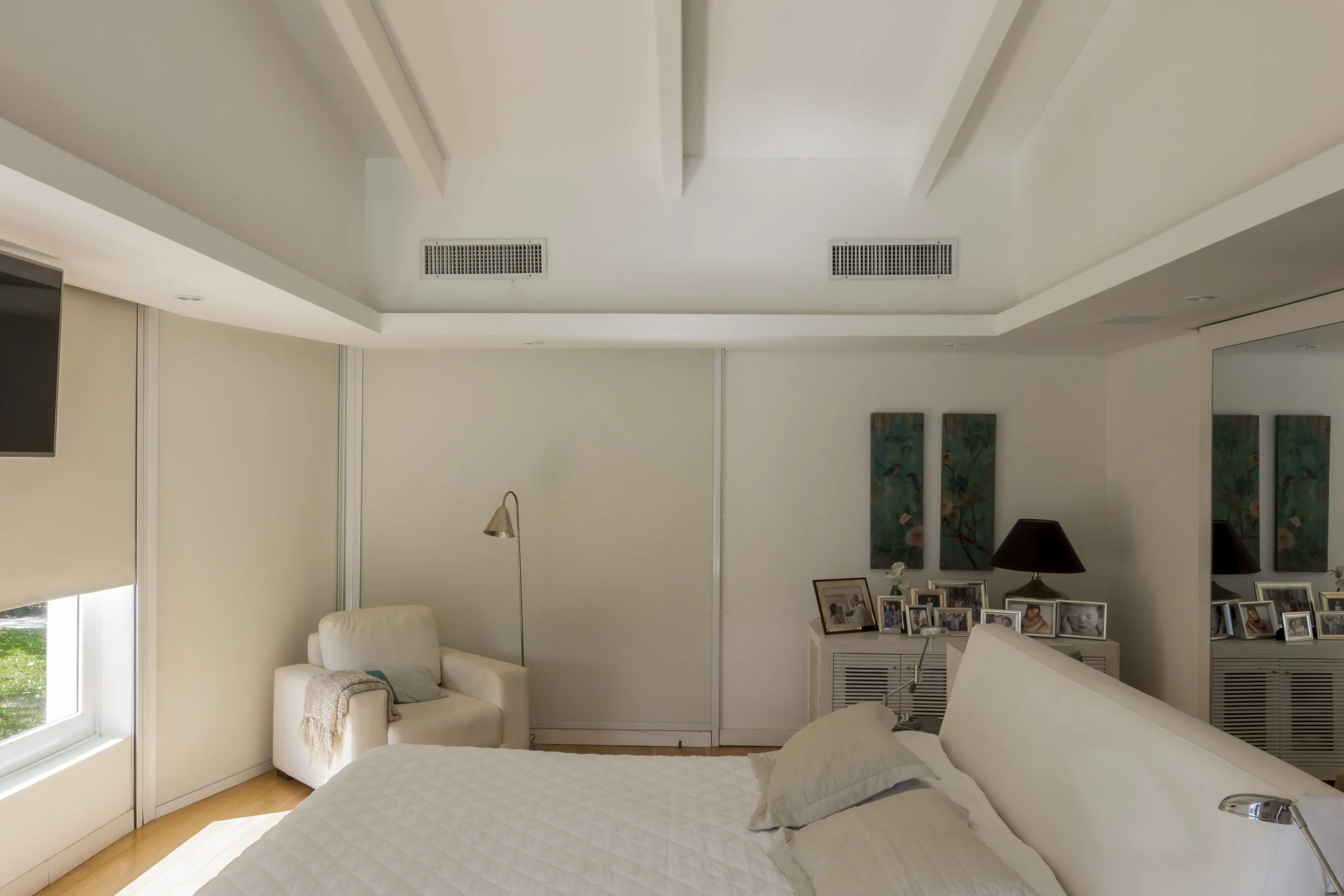 Habitación moderna con cama, sillón, lámpara, cuadros y fotos familiares.