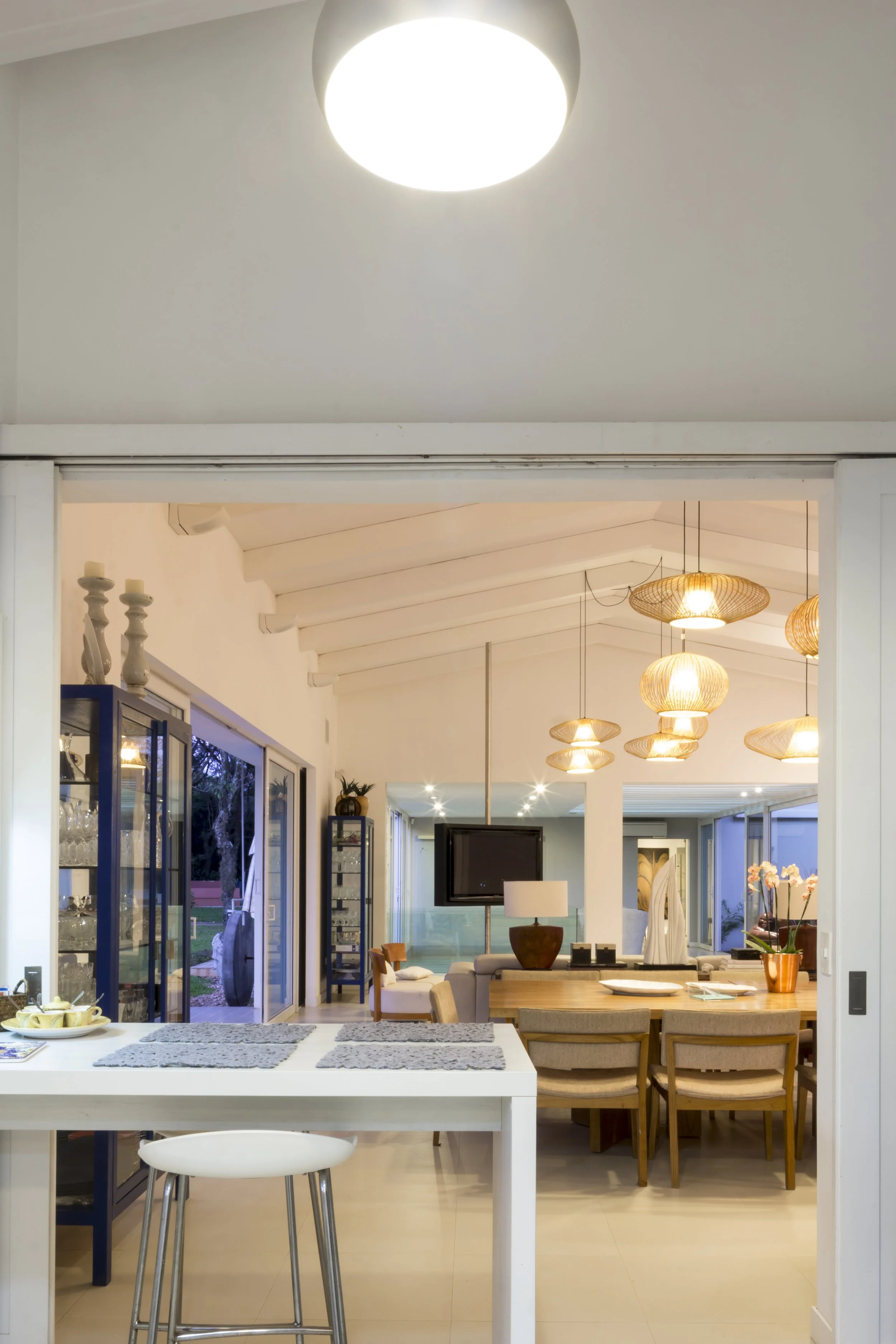 Vista de una sala y comedor modernos con lámparas de mimbre, una televisión y un comedor de madera.