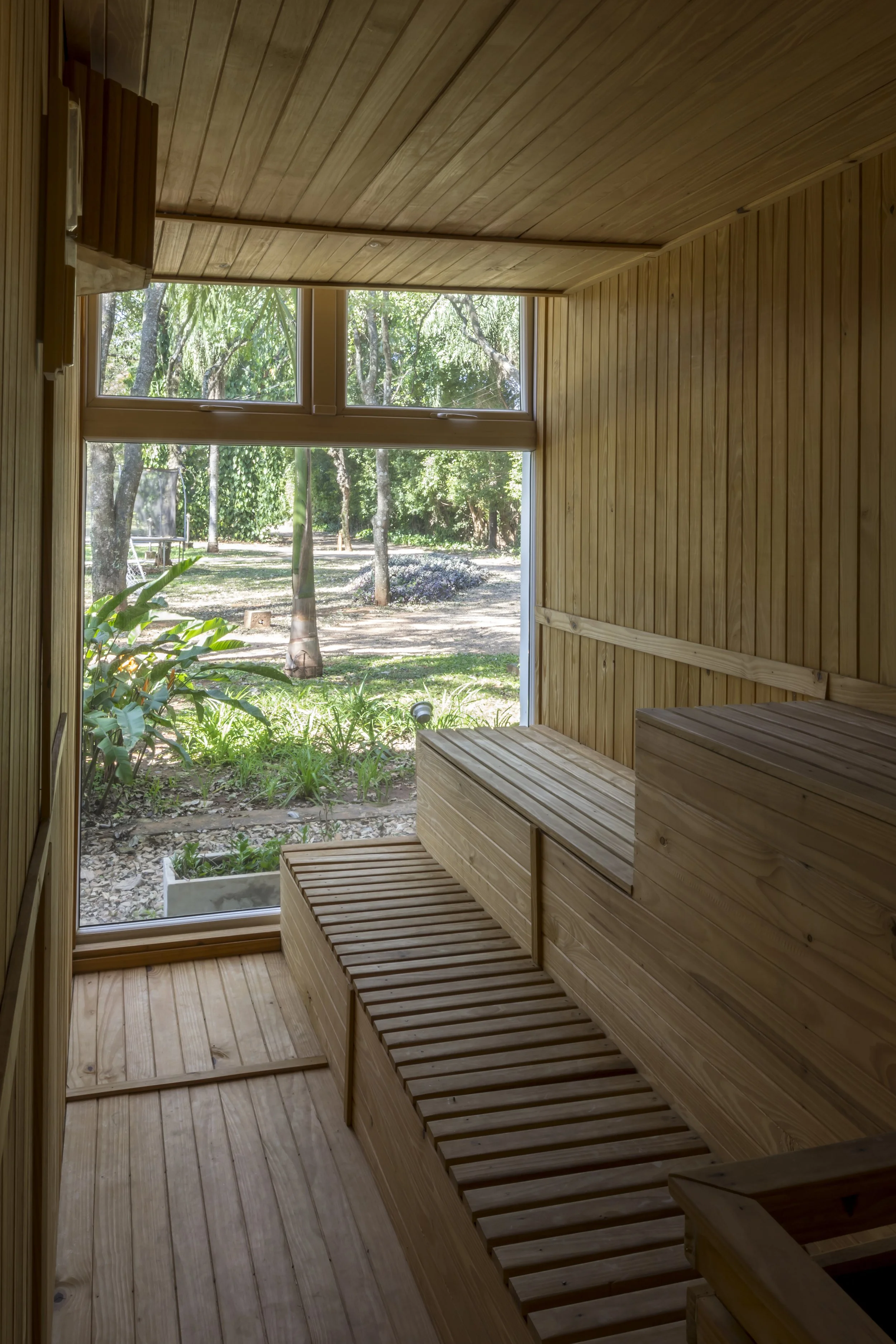 Cabina de sauna de madera con ventana grande que muestra un jardín con árboles y plantas verdes.