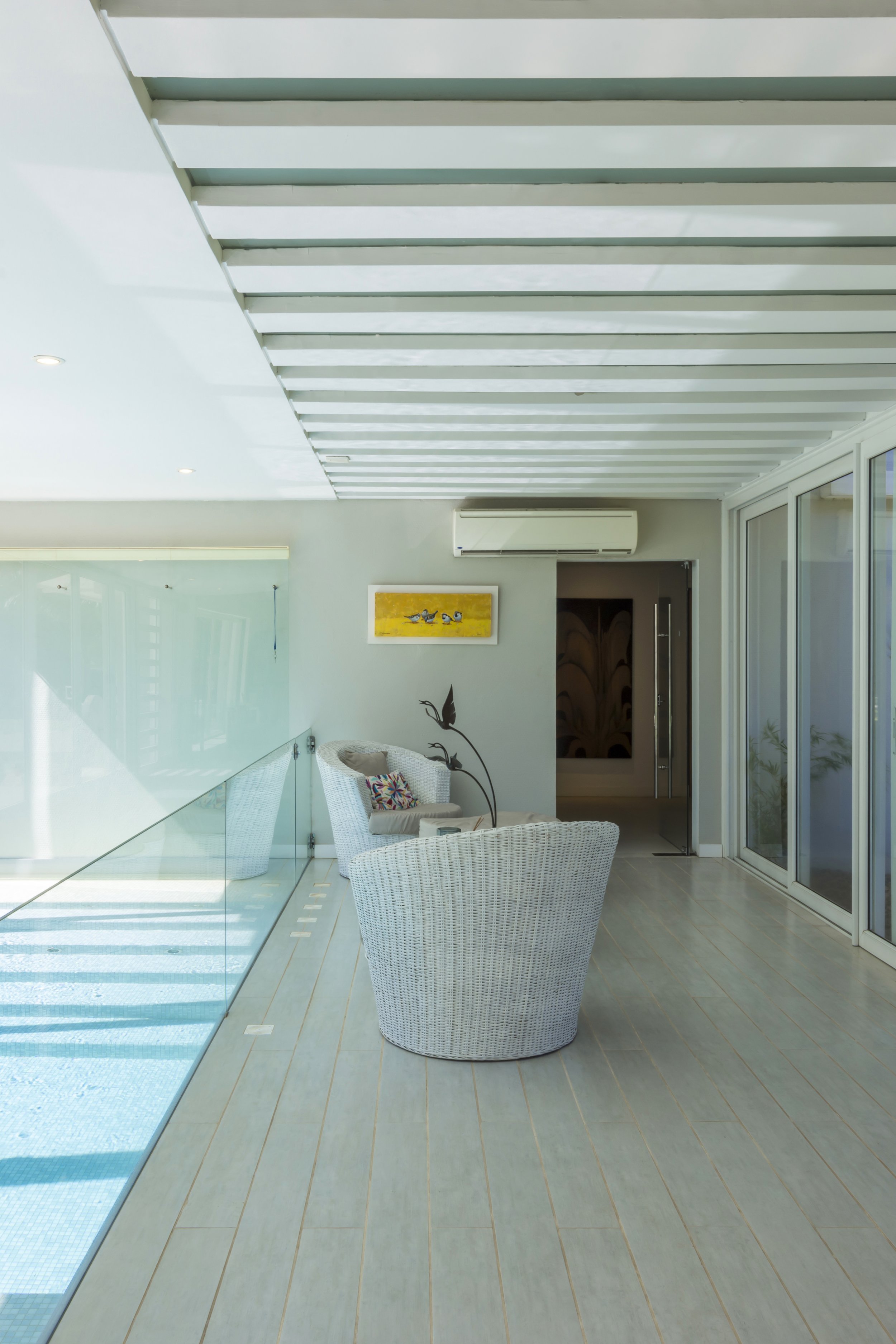 Interiores modernos con sillas blancas de mimbre, una mesa y una decoración sencilla, en una sala con ventanas grandes y un techo con vigas blancas.