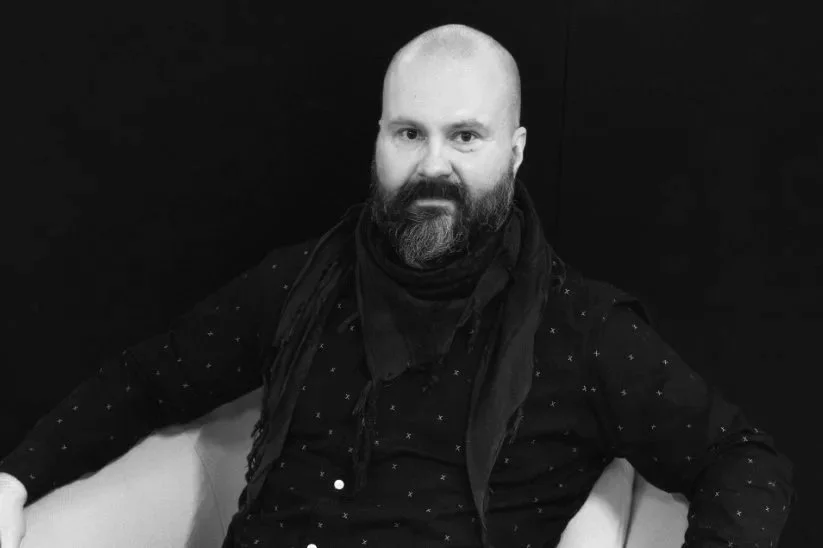 Jukka Niittymaa istuu sohvalla mustassa paidassa ja huivissa, katsoo kameraan.