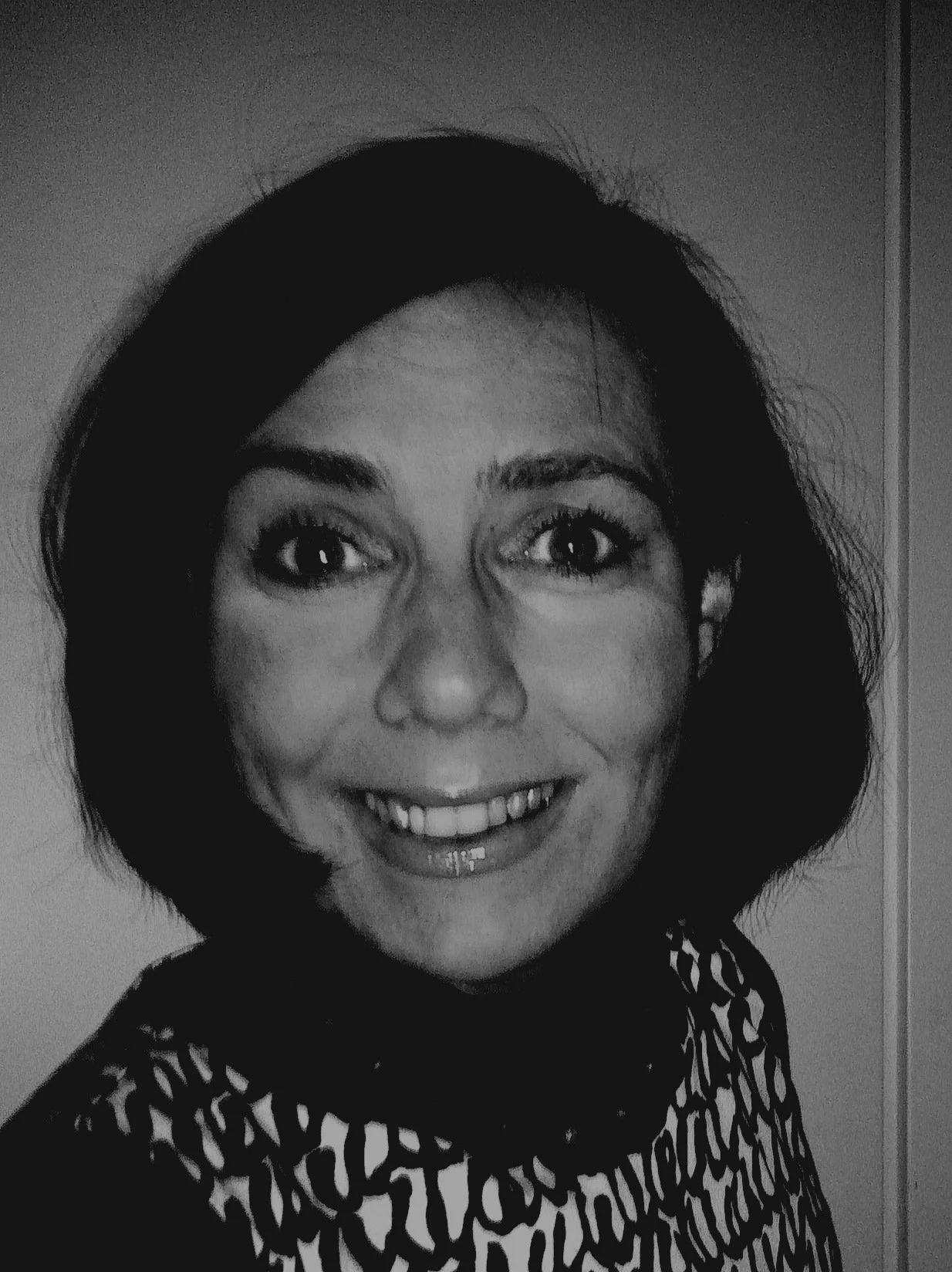 Mustavalkoinen valokuva hymyilevästä naisesta, jolla on lyhyt tummatukka ja kuvioitu yläosa.